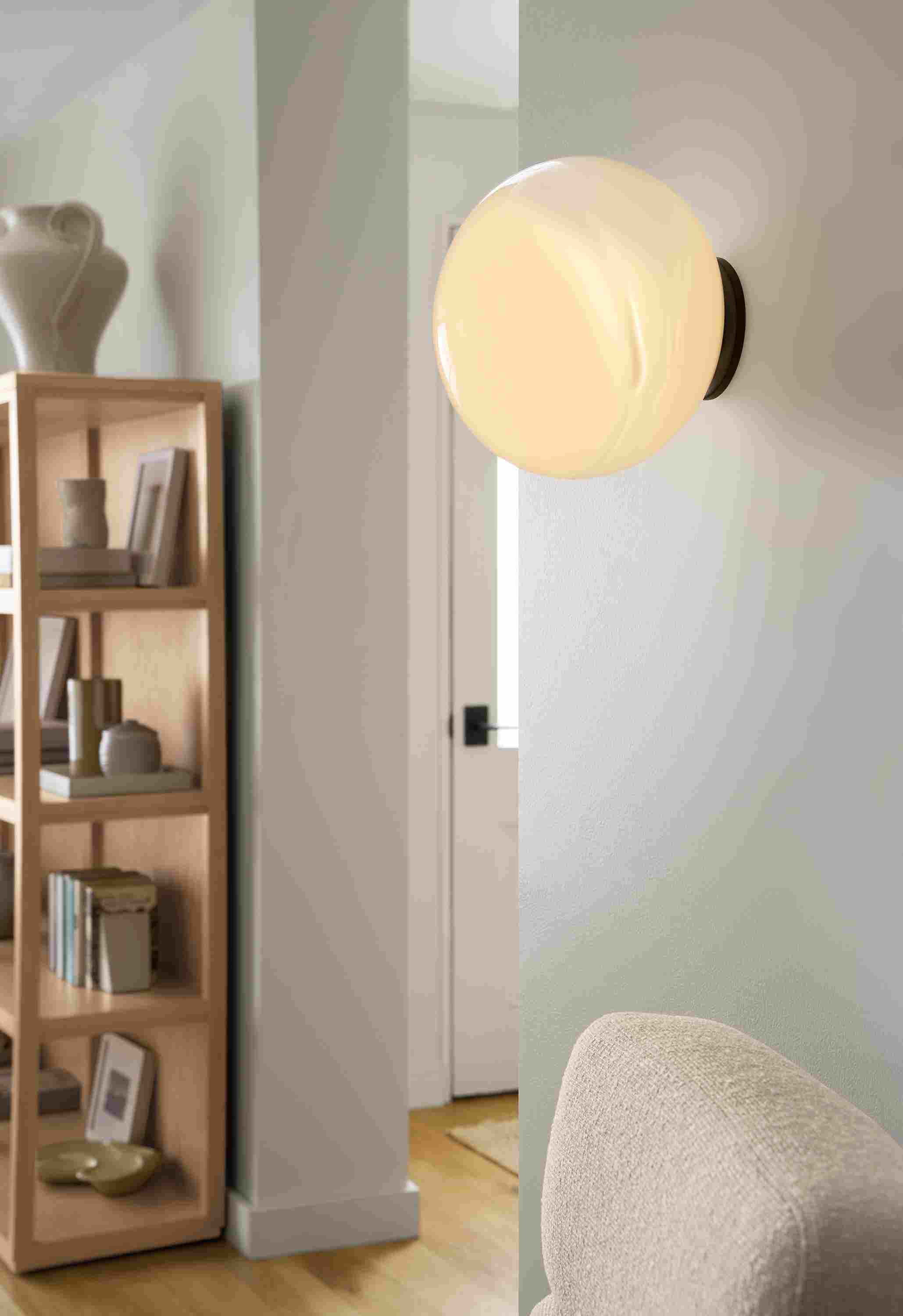 Living room with detail of Osiris wall sconce in graphite with  opal globe and Fable bookcase in rye on red oak.