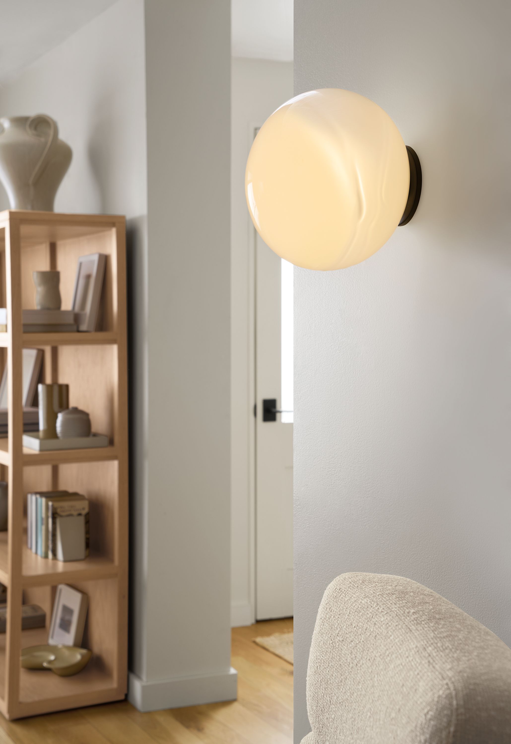 Living room with detail of Osiris wall sconce in graphite with  opal globe and Fable bookcase in rye on red oak.