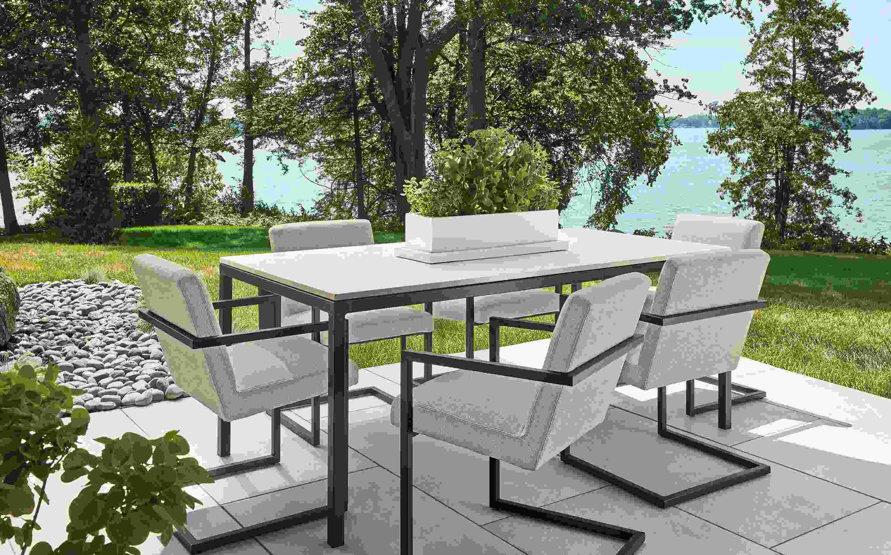 Lakeside patio with Parsone outdoor table in graphite with marbled beige quartz and 6 Finn chairs.