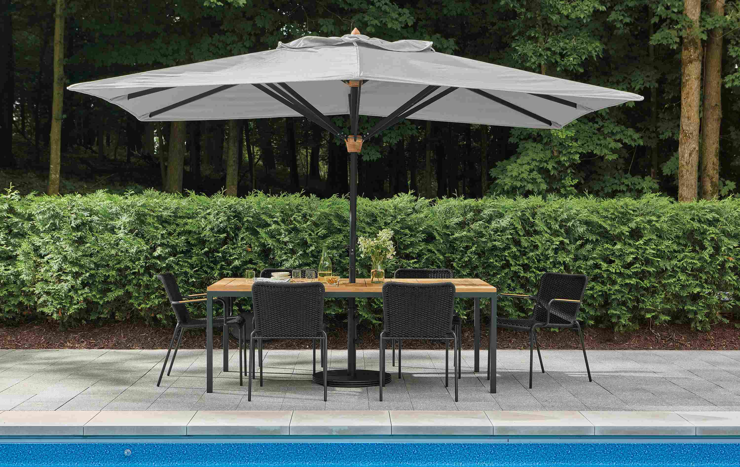 Pool patio with Parsons table in graphite and teak heartwood and banda umbrella in Halo Grey.