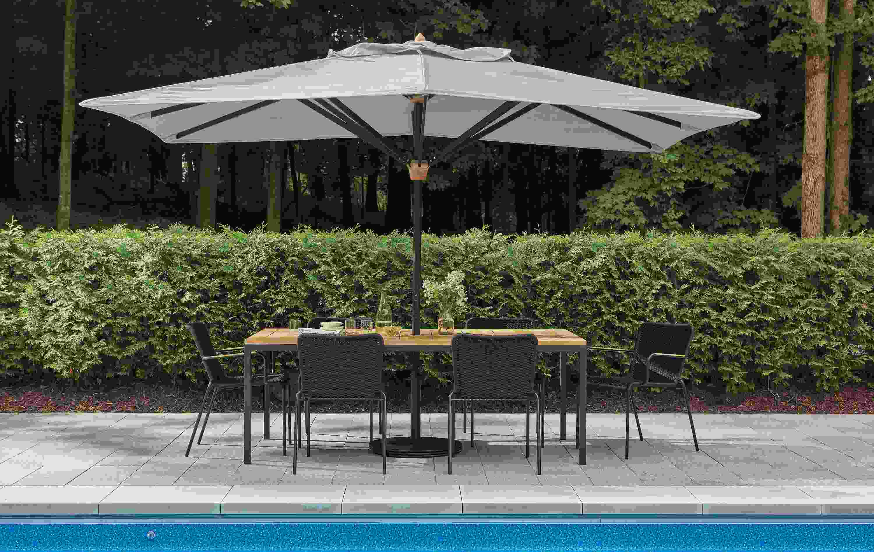 Pool patio with Parsons table in graphite and teak heartwood and banda umbrella in Halo Grey.