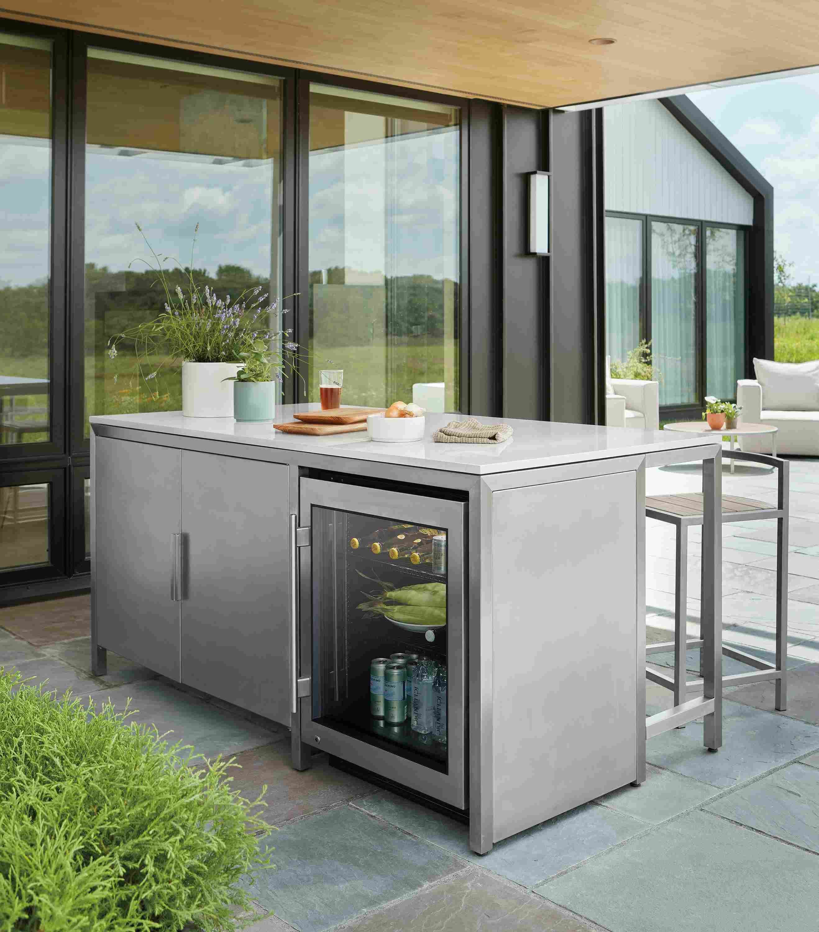 Patio area with parsons outdoor counter table with 2 door cabinet and glass door fridge in stainless steel.