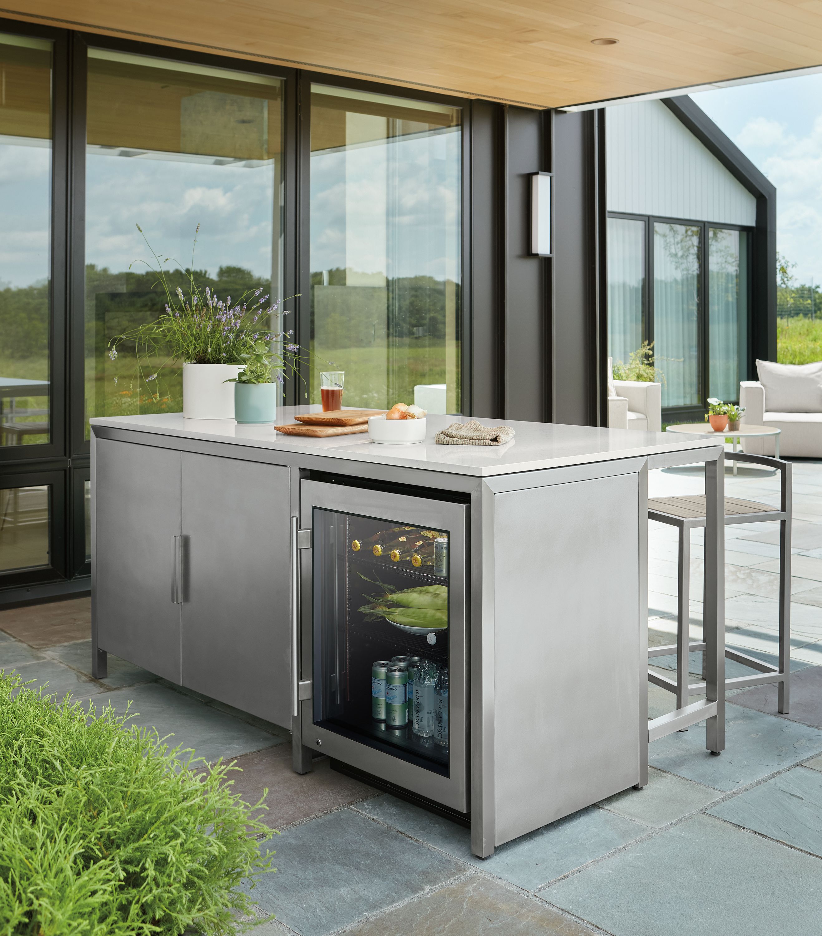 Patio area with parsons outdoor counter table with 2 door cabinet and glass door fridge in stainless steel.