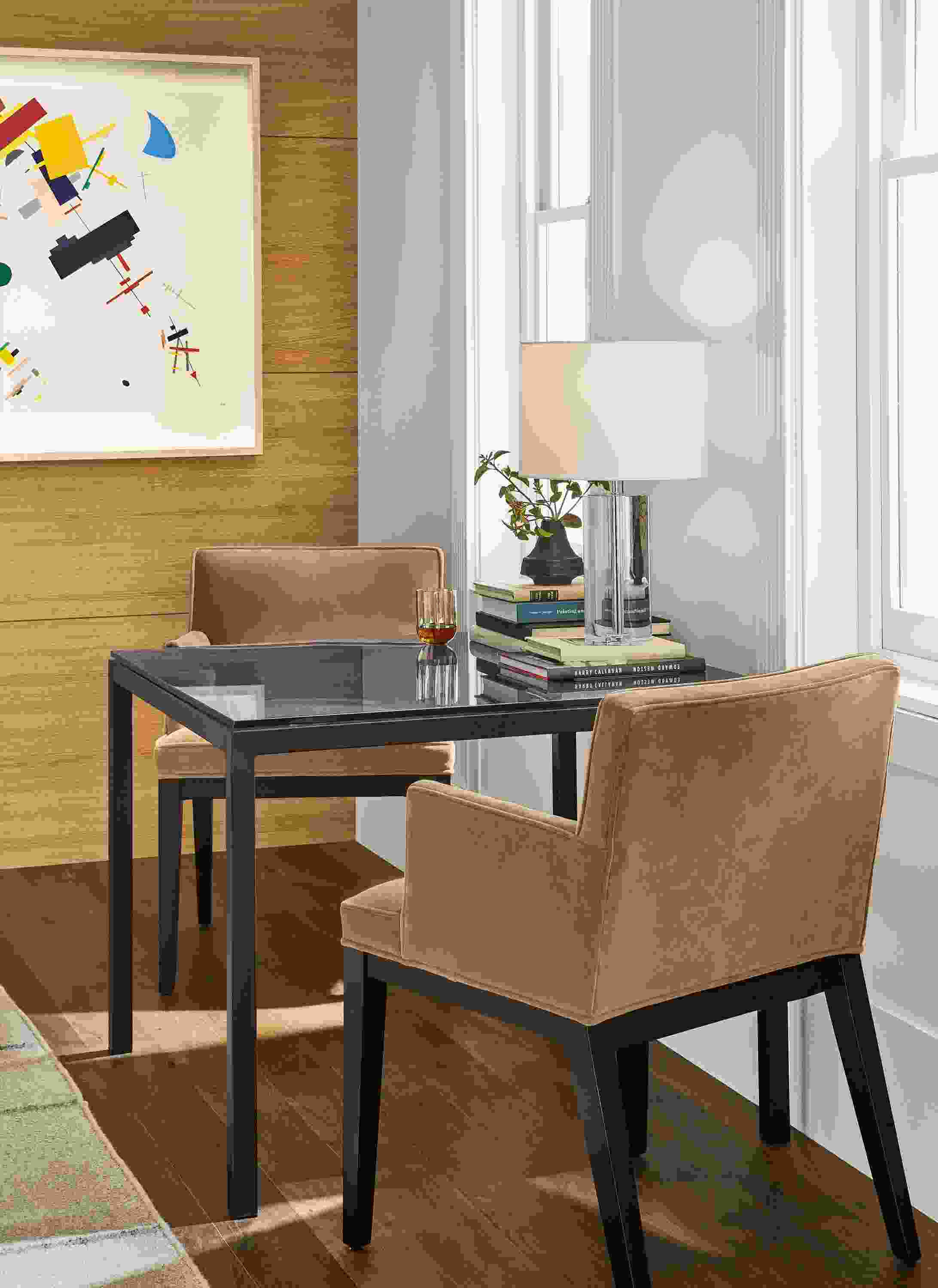 Detail of Parsons table with smoke glass top and natural steel base with two Ansel arm chairs.