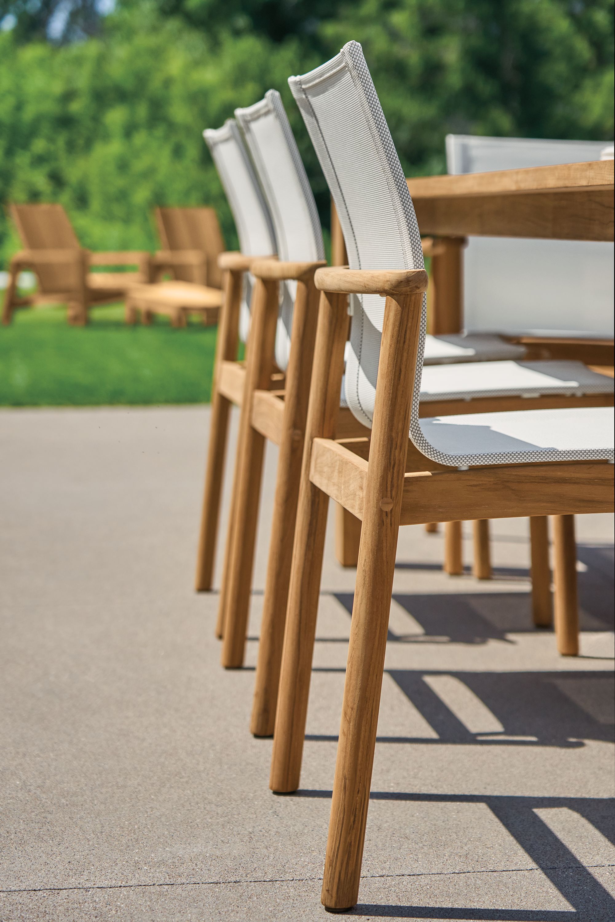 Low angle detail of 3 Peri side chairs in teak heartwood with salt outdoor sling.