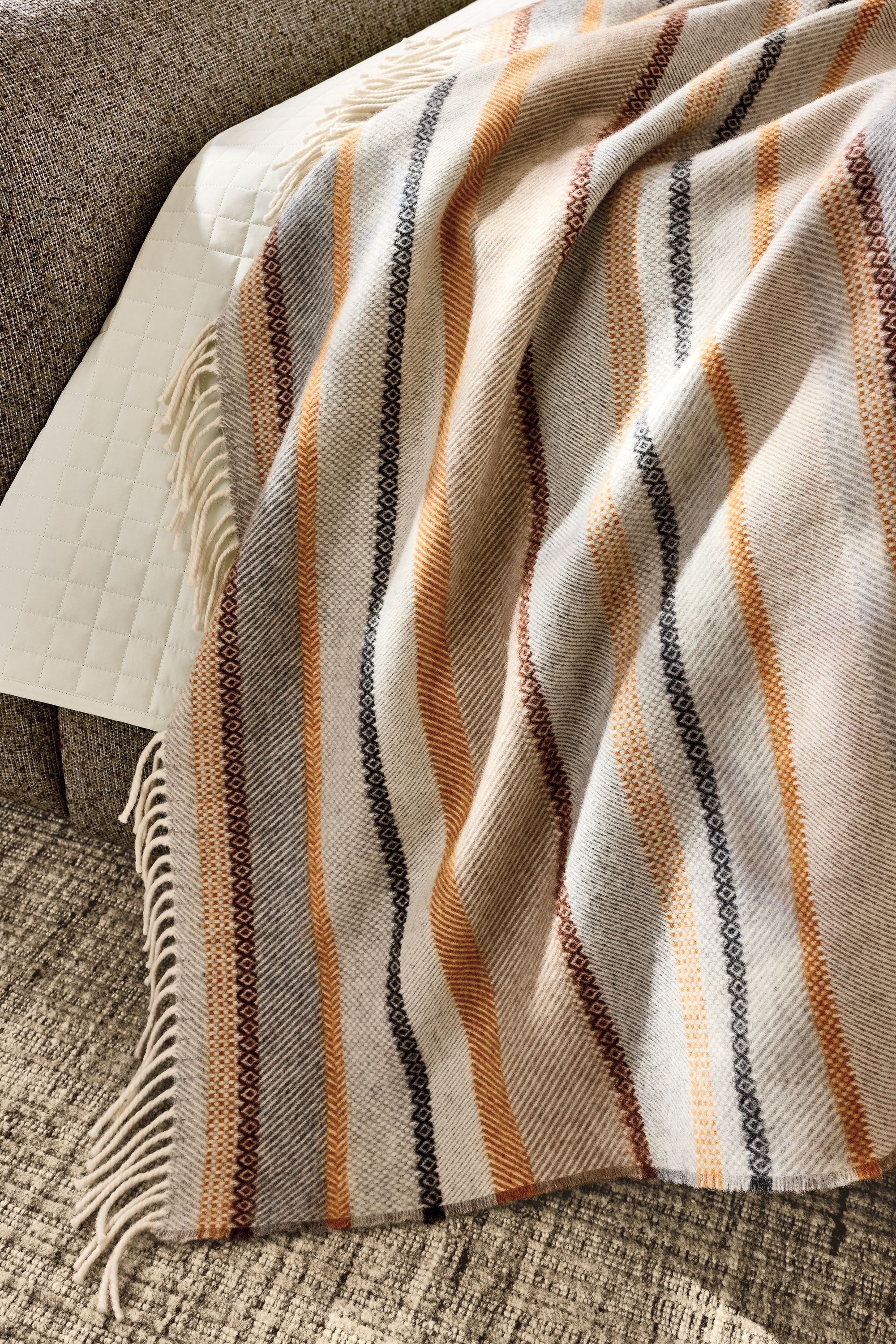 Detail of a Picton throw blanket in Amber on a Rue bed in conley mink and Artis rug in stone.