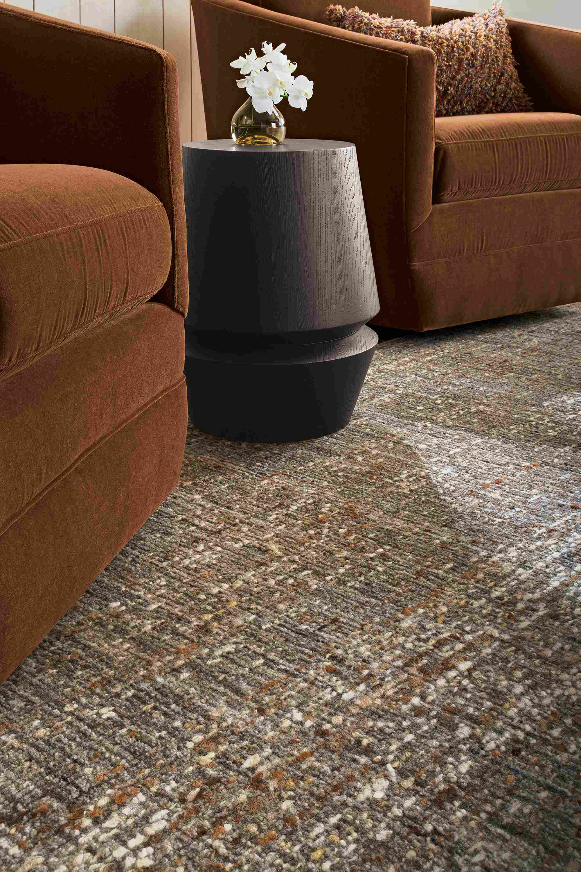Low-angle detail of a Ravani rug in charcoal, 2 Ford swivel chairs in Redding Nutmeg and Nyla stool in charcoal.