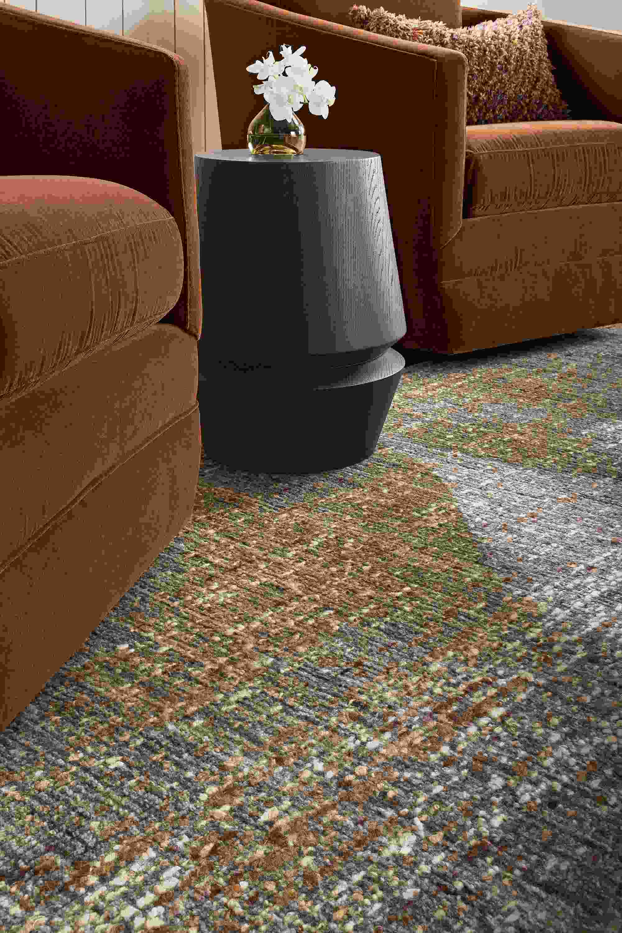 Low-angle detail of a Ravani rug in charcoal, 2 Ford swivel chairs in Redding Nutmeg and Nyla stool in charcoal.