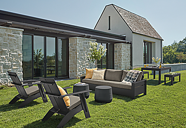 Rayo Sofa and Emmet Tall Lounge Chairs in black with Pelham charcoal cushions and Cusp Stool in Grey on a lawn.