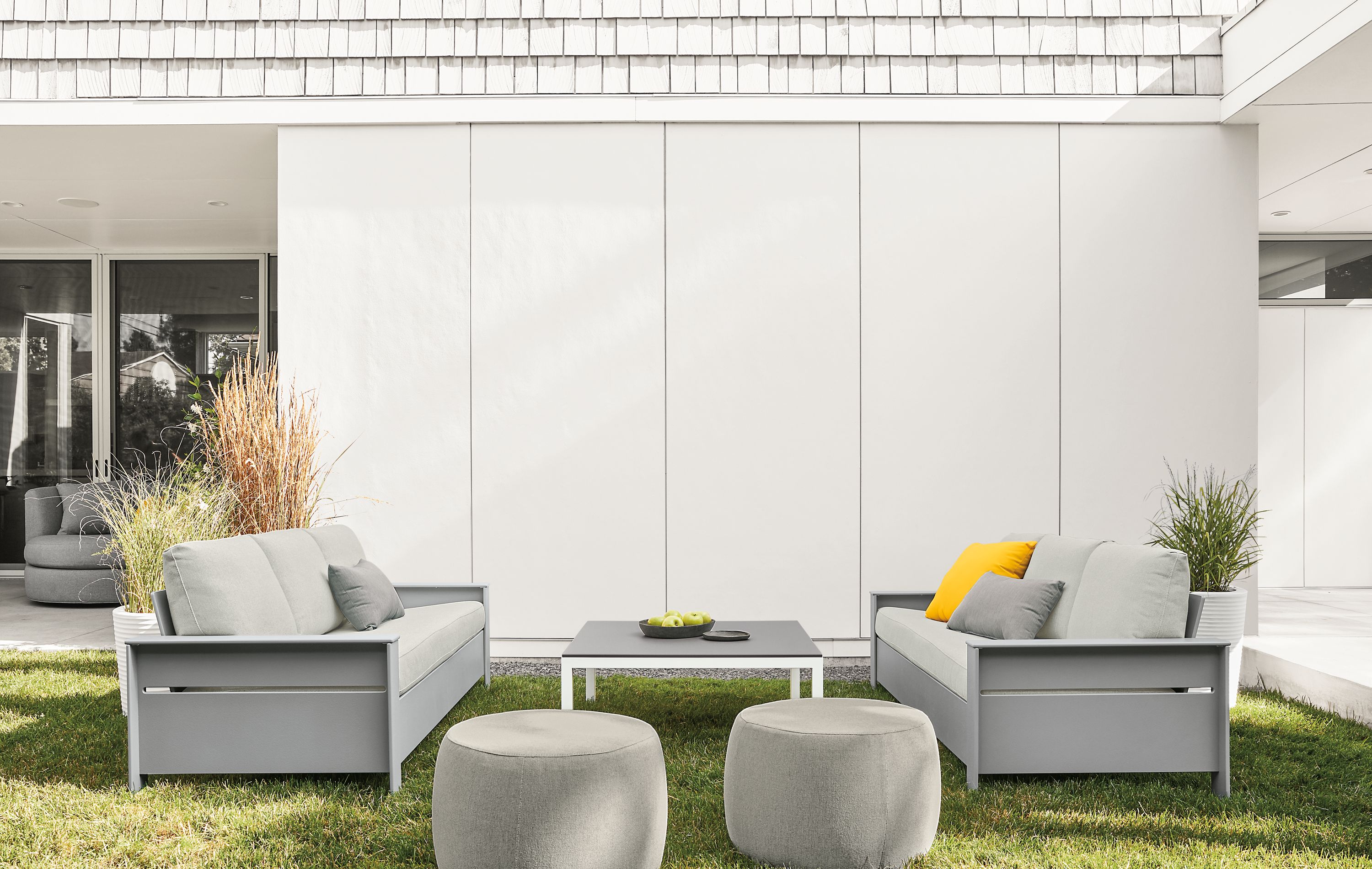 Two Rayo sofas Light Grey with Mist Grey cushions and 2 Boyd ottomans in Mist Grey in lawn.