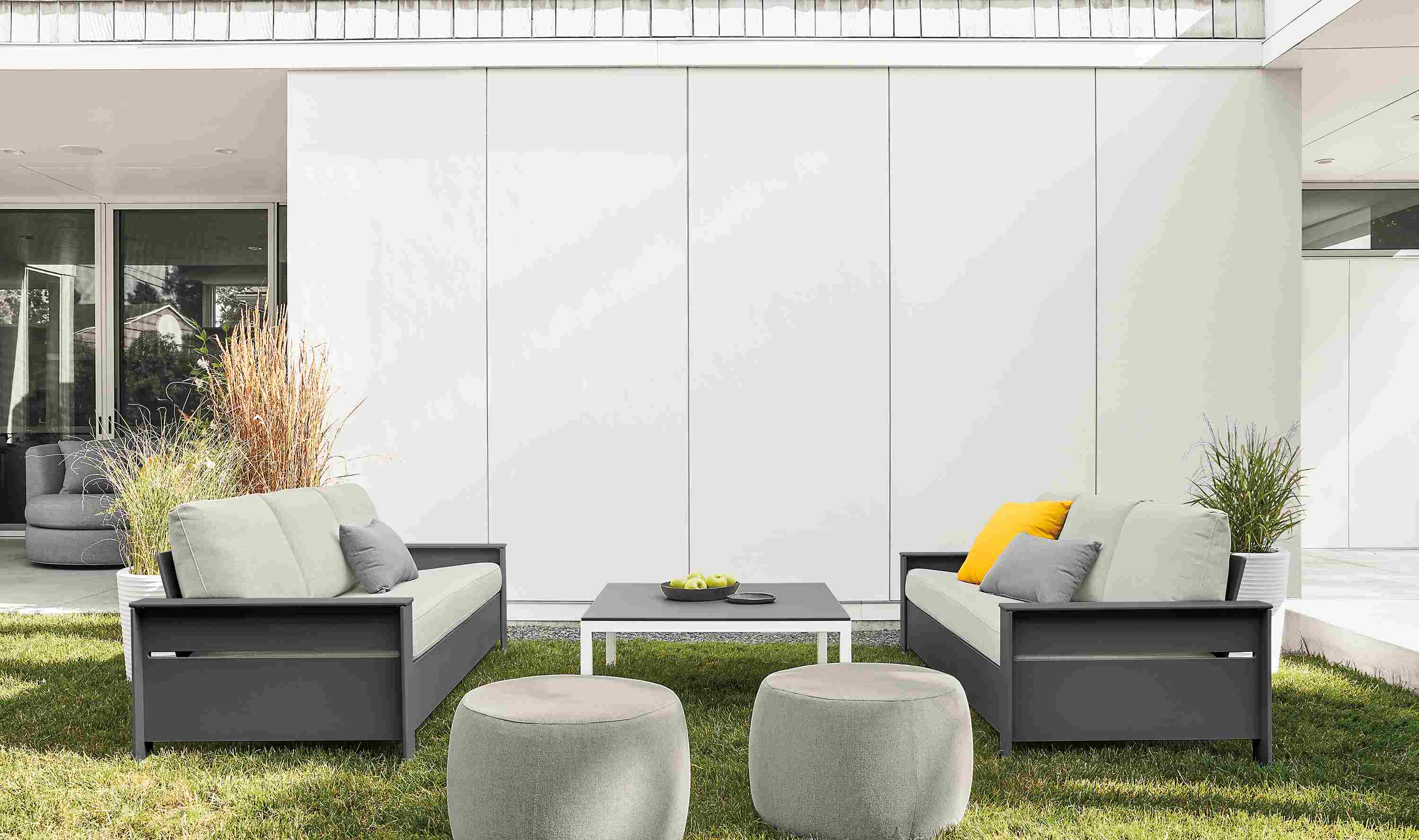 Lawn seating area with 2 Rayo sofas in Mist Grey and Grey HDPE and 2 Boyd ottomans in Mist Grey.