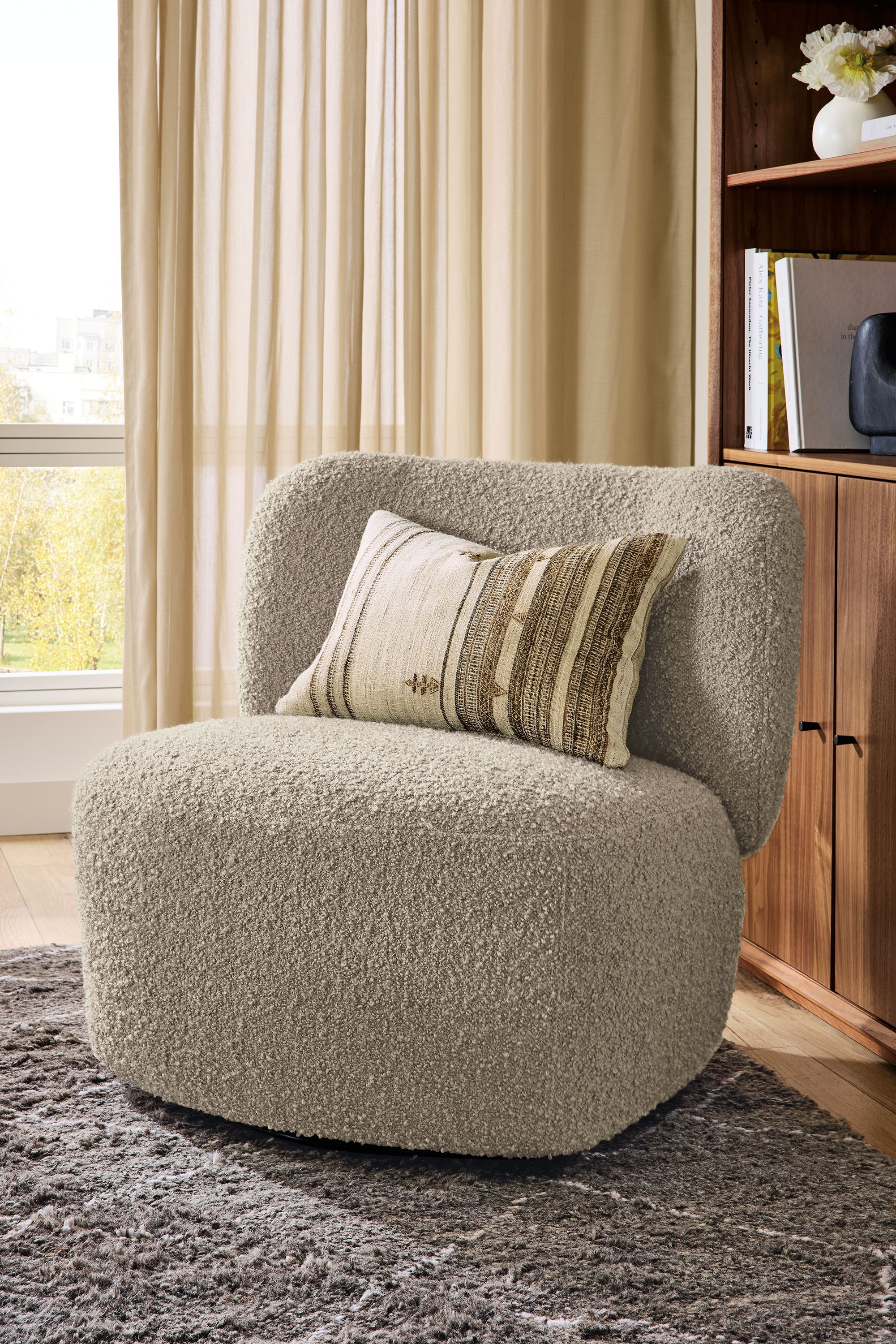 Detail of a Rory swivel chair in Dornick Otter, Kalindi 9 by 12 rug in charcoal and Bhujodi pillow in ivory.