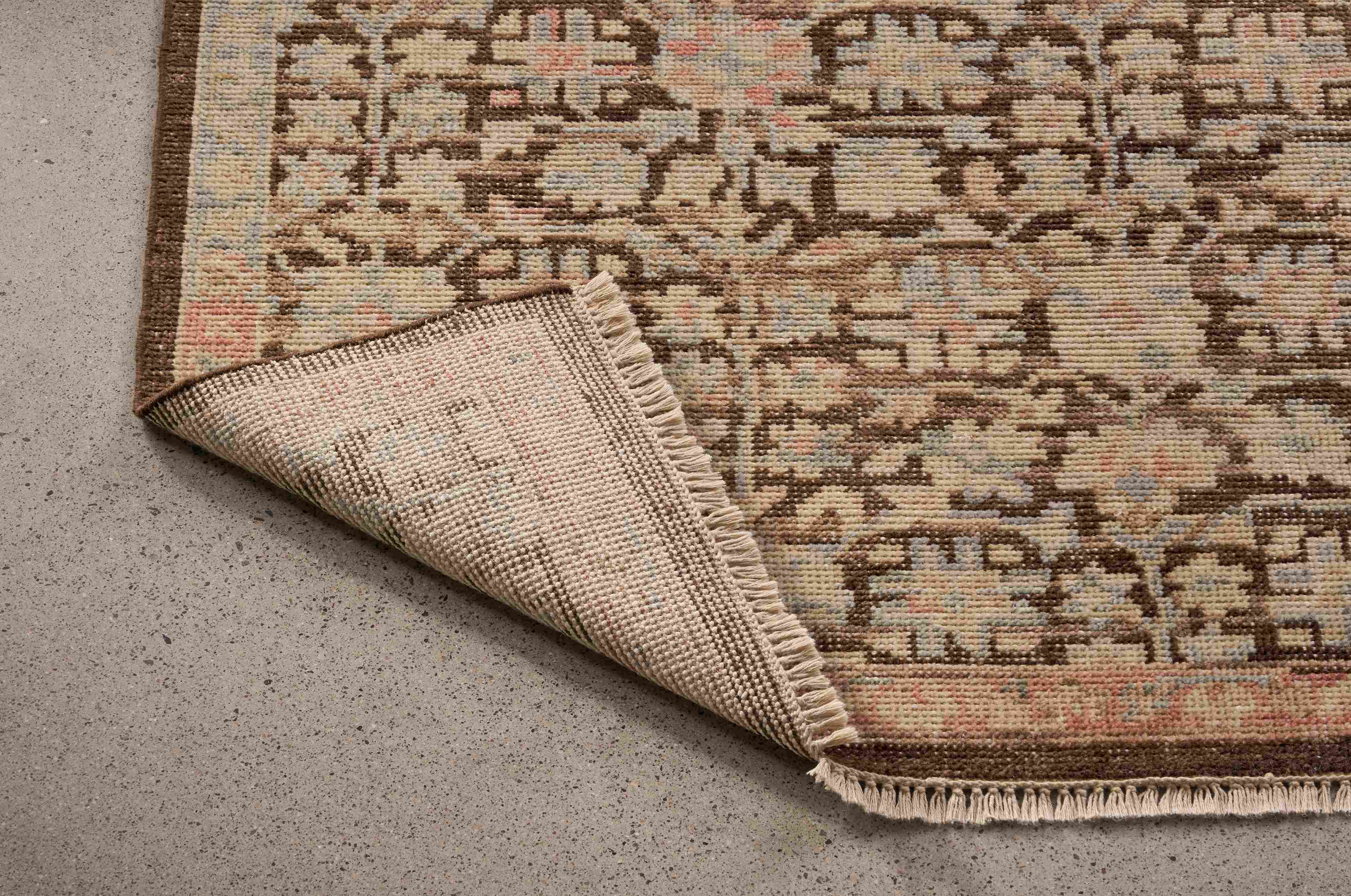 Detail of Rosalie 8 by 10 rug in petal shown with corner flipped up to show underside of rug.