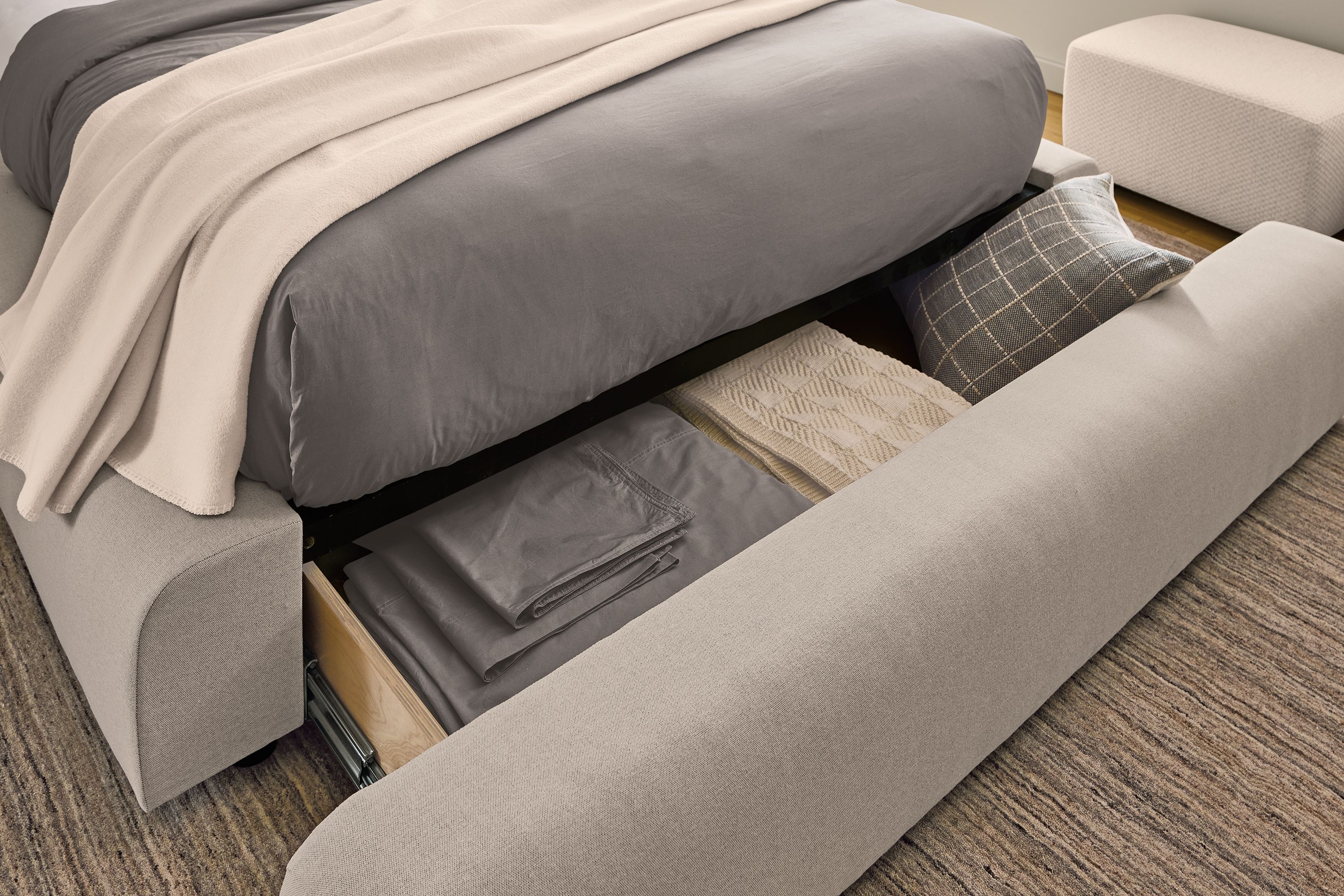 Open drawer with sheets, blankets and pillows inside  on a Rue Queen storage bed in Myers Oatmeal.
