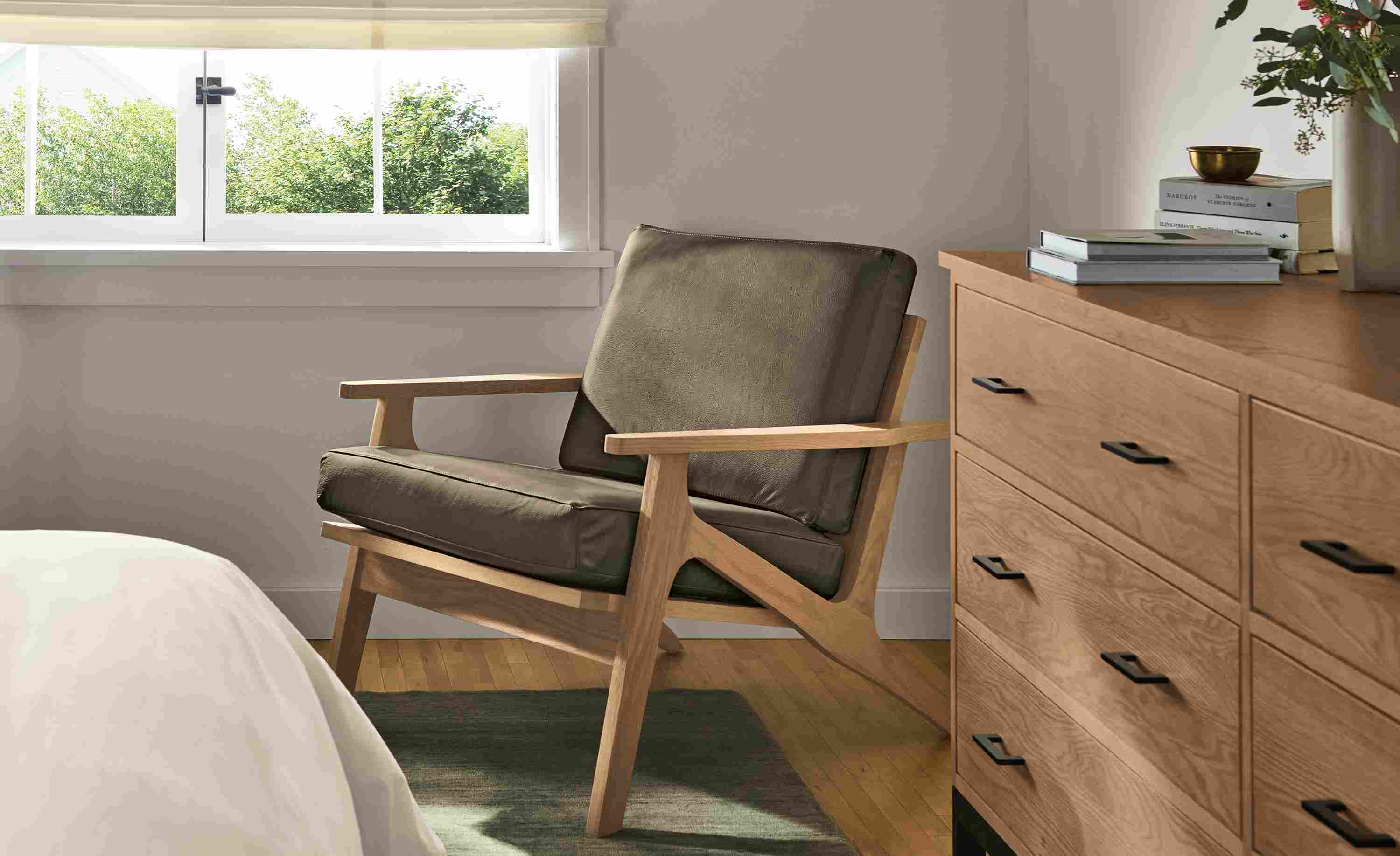 Bedroom with Sanna chair in Pesaro Mink Leather and rye on red oak and Nomad rug in Olive.