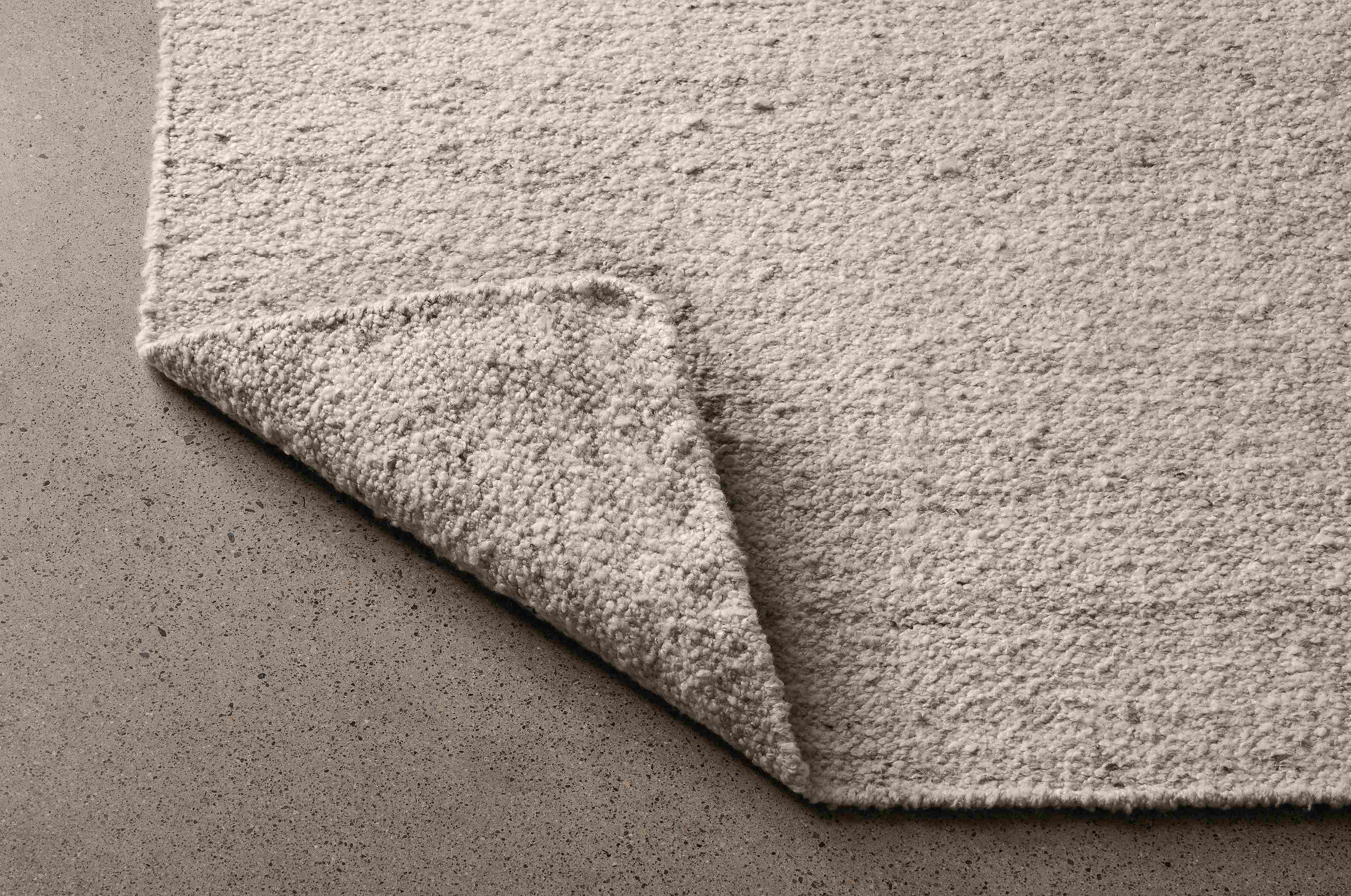 Detail of Sefton 8 by 10 rug in cement shown with corner flipped up to show underside of rug.