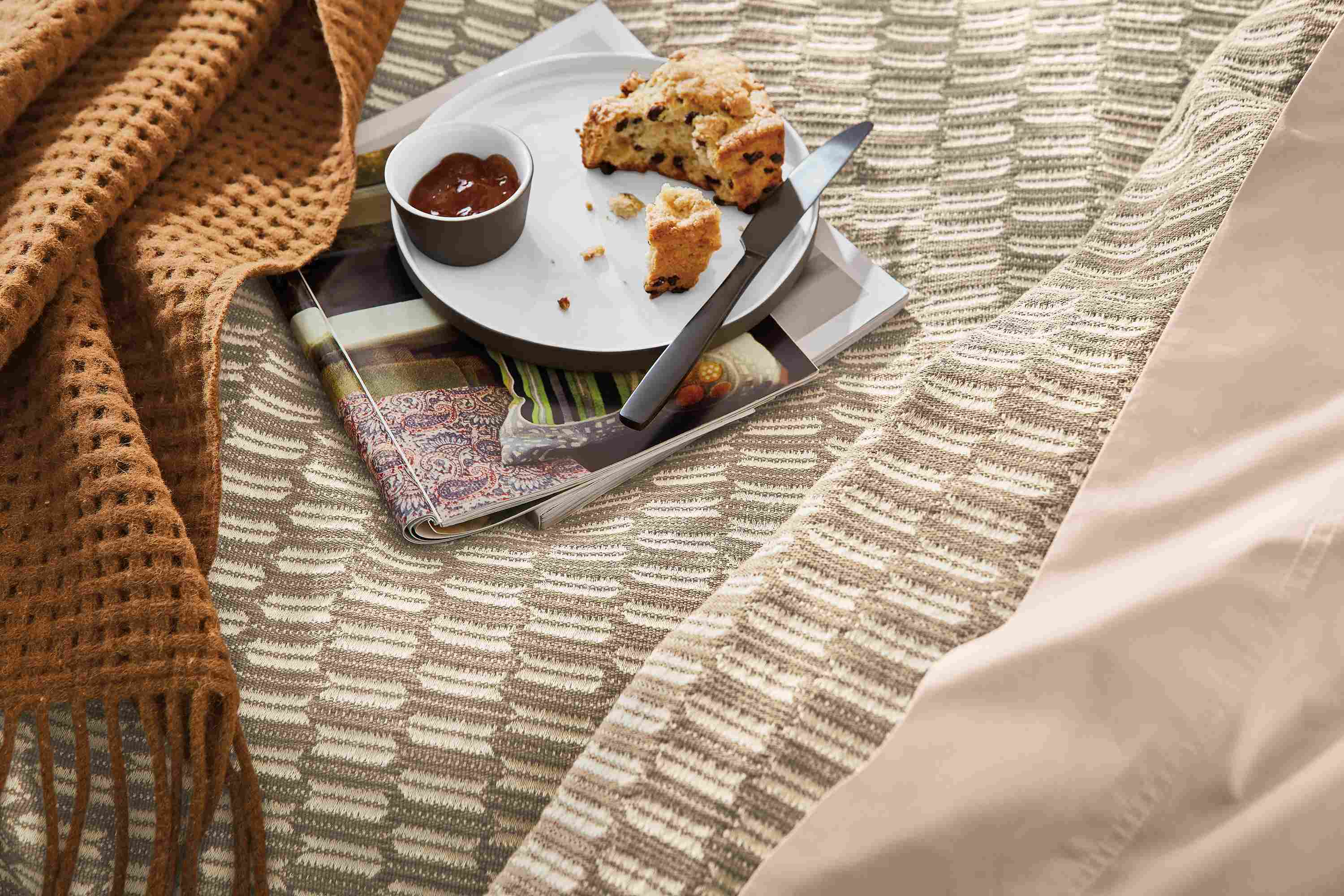 detail of lagoa plate with breakfast sitting on magazines on bed.