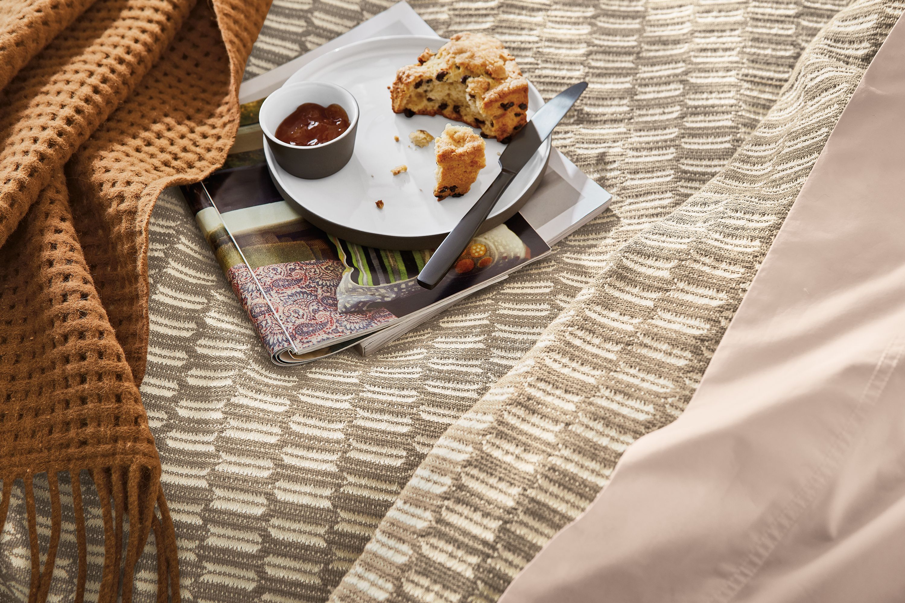 detail of lagoa plate with breakfast sitting on magazines on bed.
