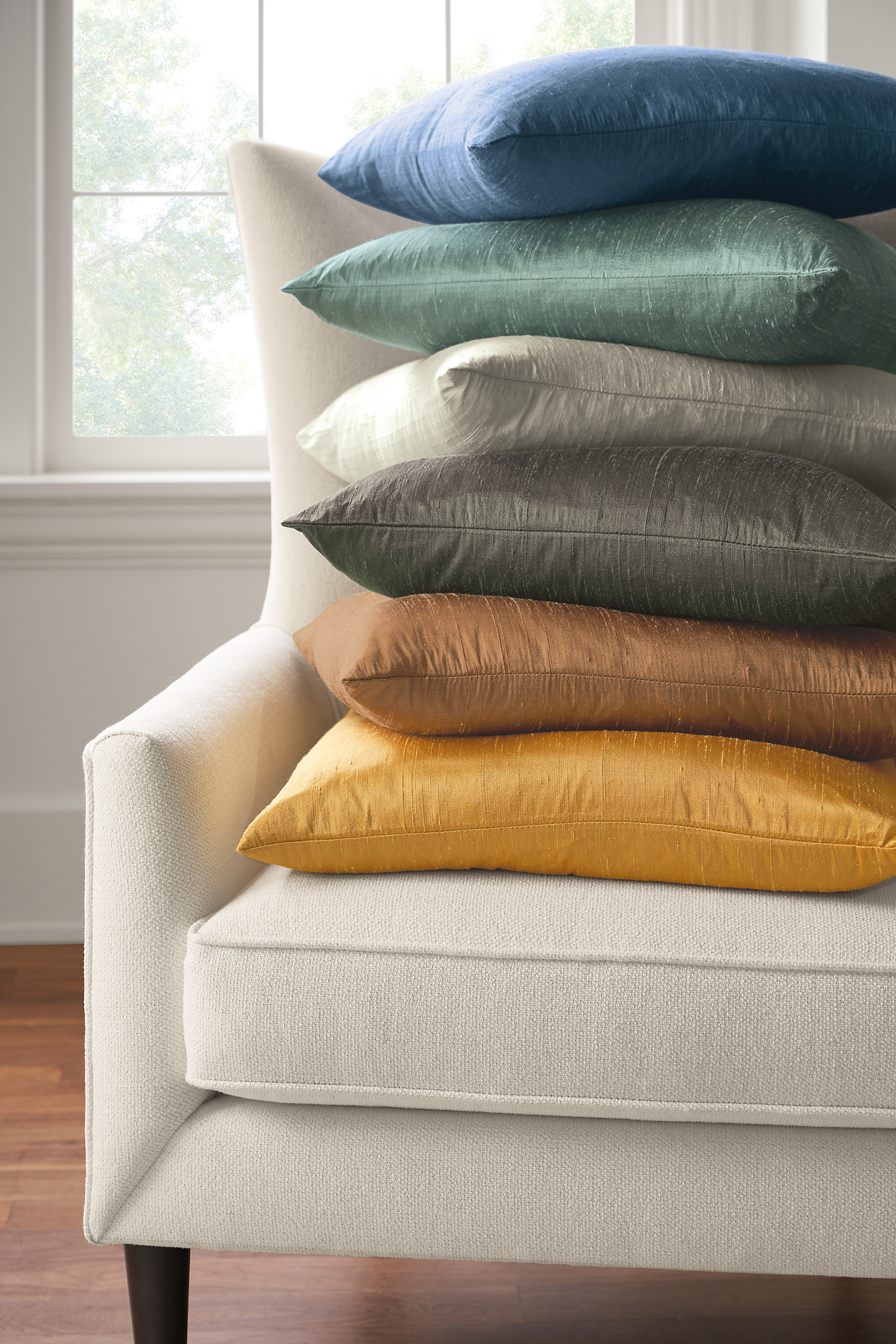 six silk pillows of various colors on a chair.