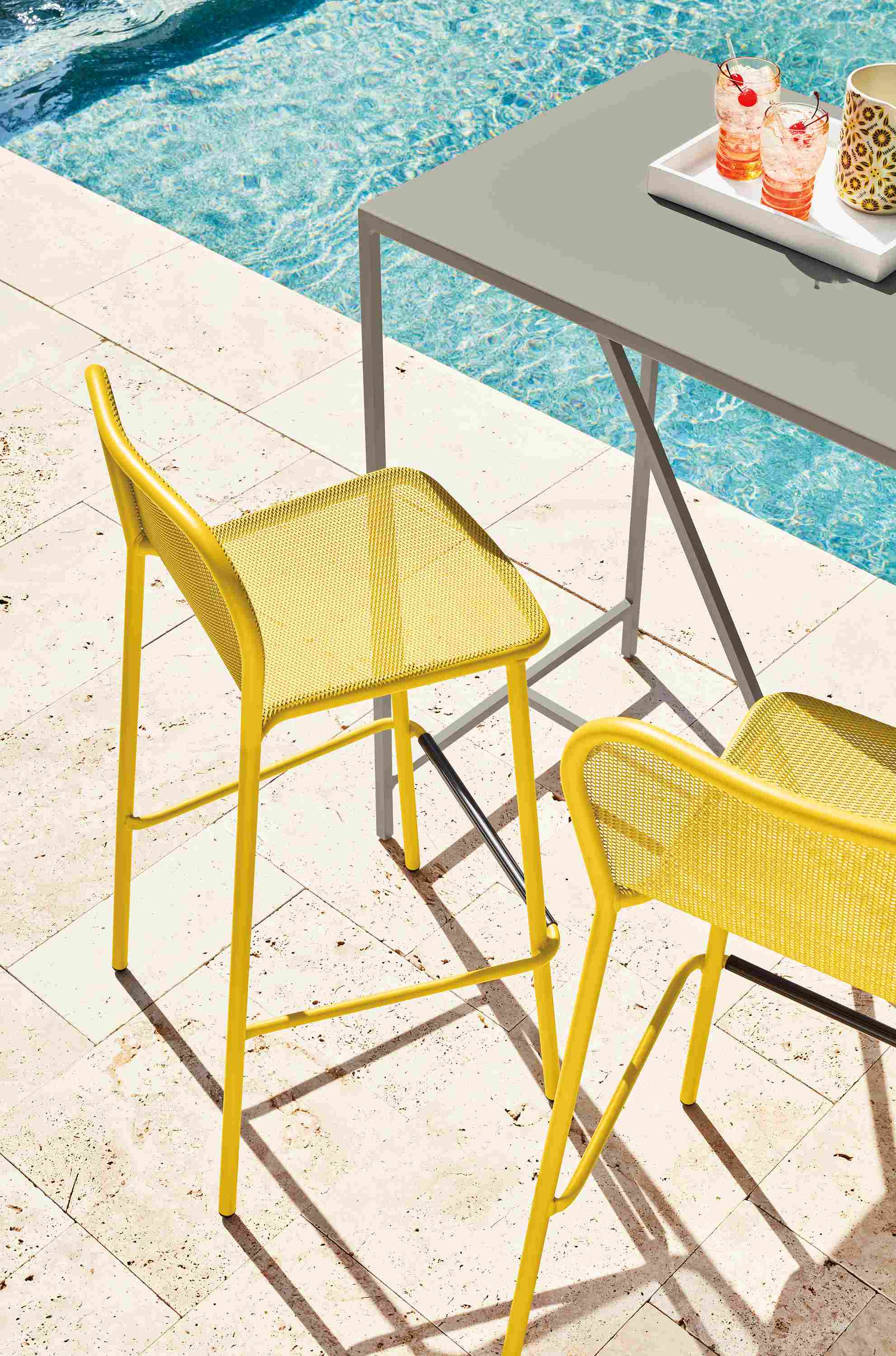 Poolside view of 2 Theo outdoor bar stools in saffron with Slim outdoor bar table in taupe.