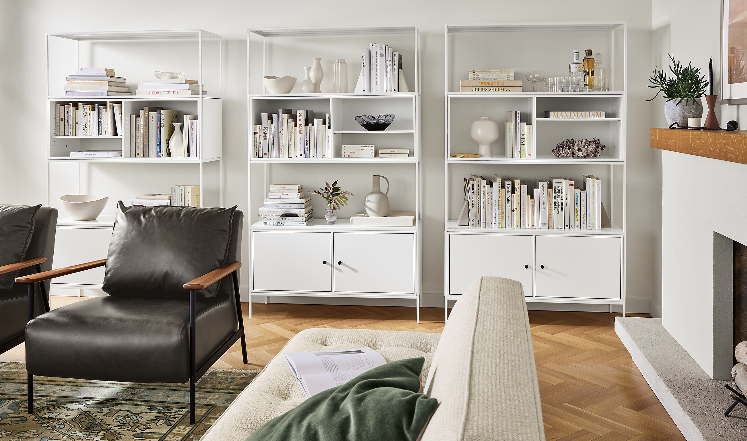 Living room with 3 slim 42 wide bookcases in white, Xavier chair in Palermo Charcoal leather, and Kayseri rug in Moss.