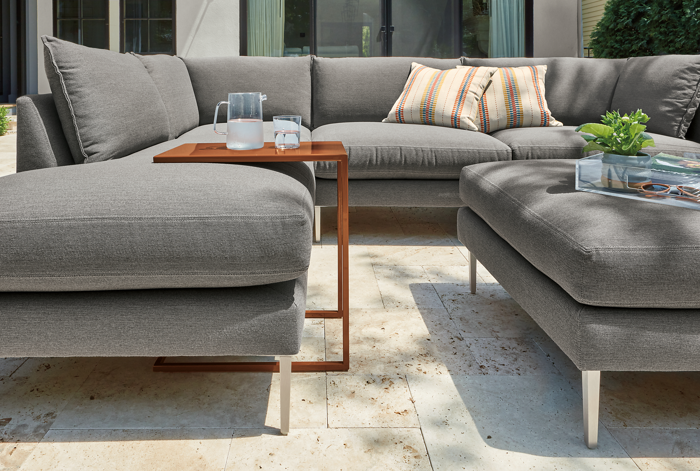 Slim outdoor c-table in cognac with Palm sectional and ottoman in Pelham grey fabric.
