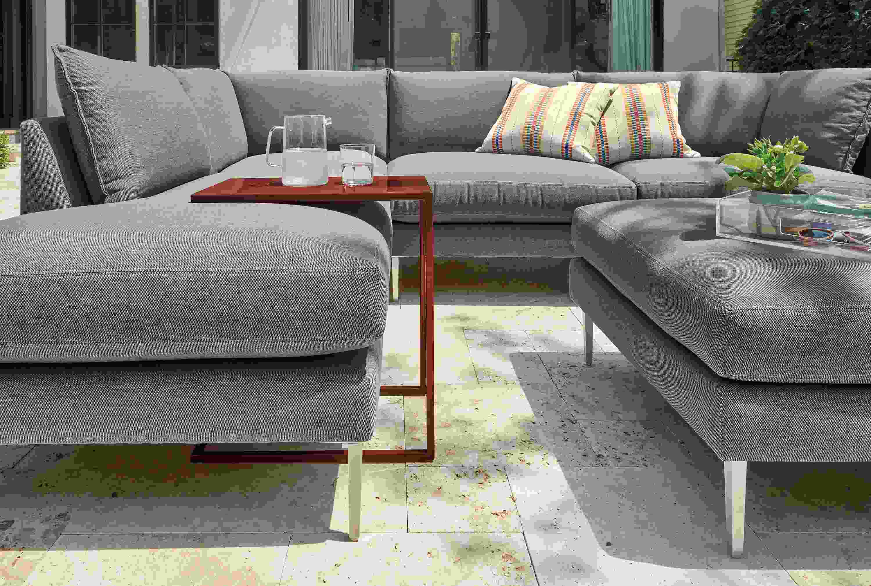 Slim outdoor c-table in cognac with Palm sectional and ottoman in Pelham grey fabric.