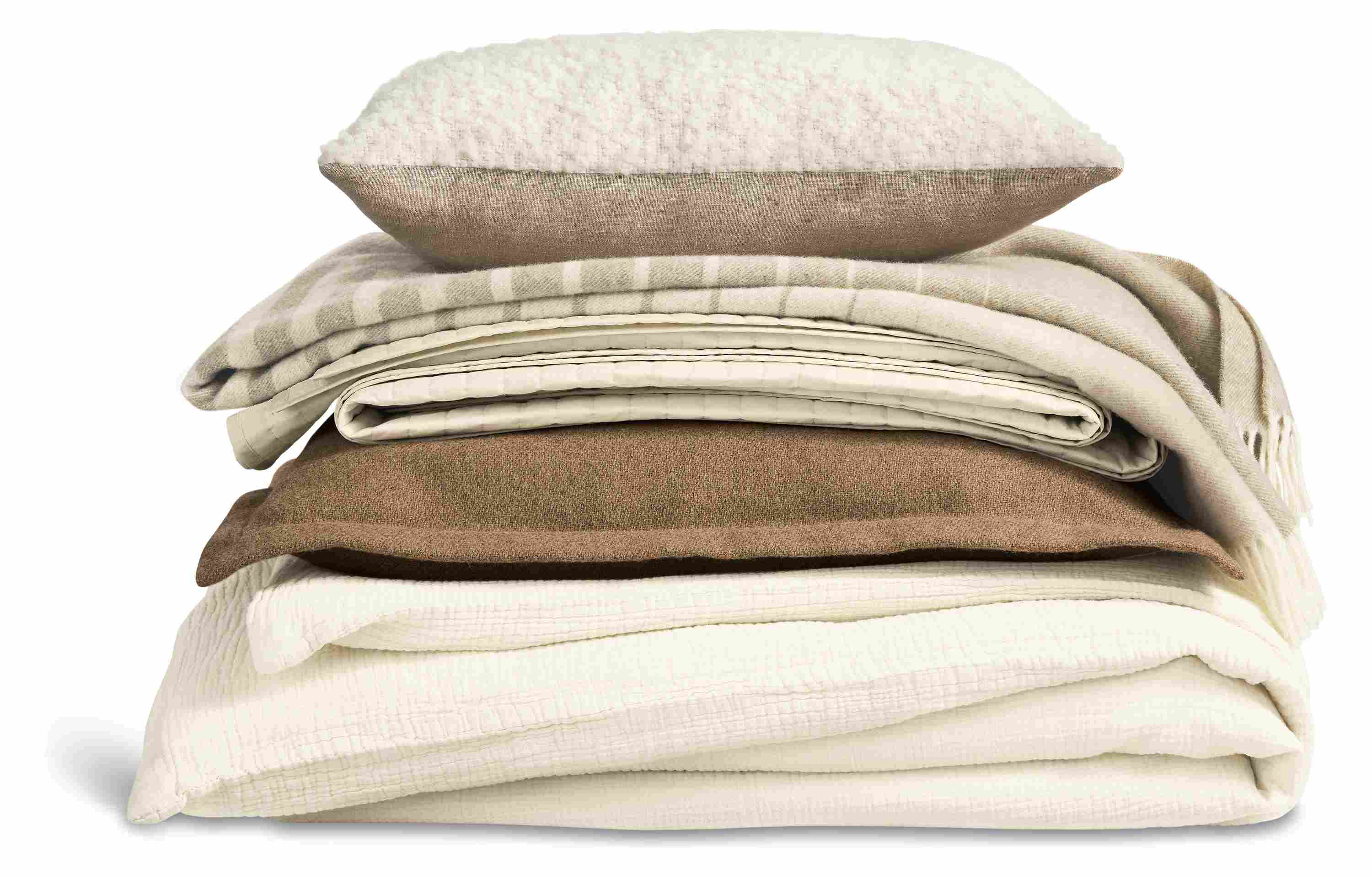 Stack of bedding with strand duvet set in ecru, washable wool euro sham in camel and percale coverlet in ecru.