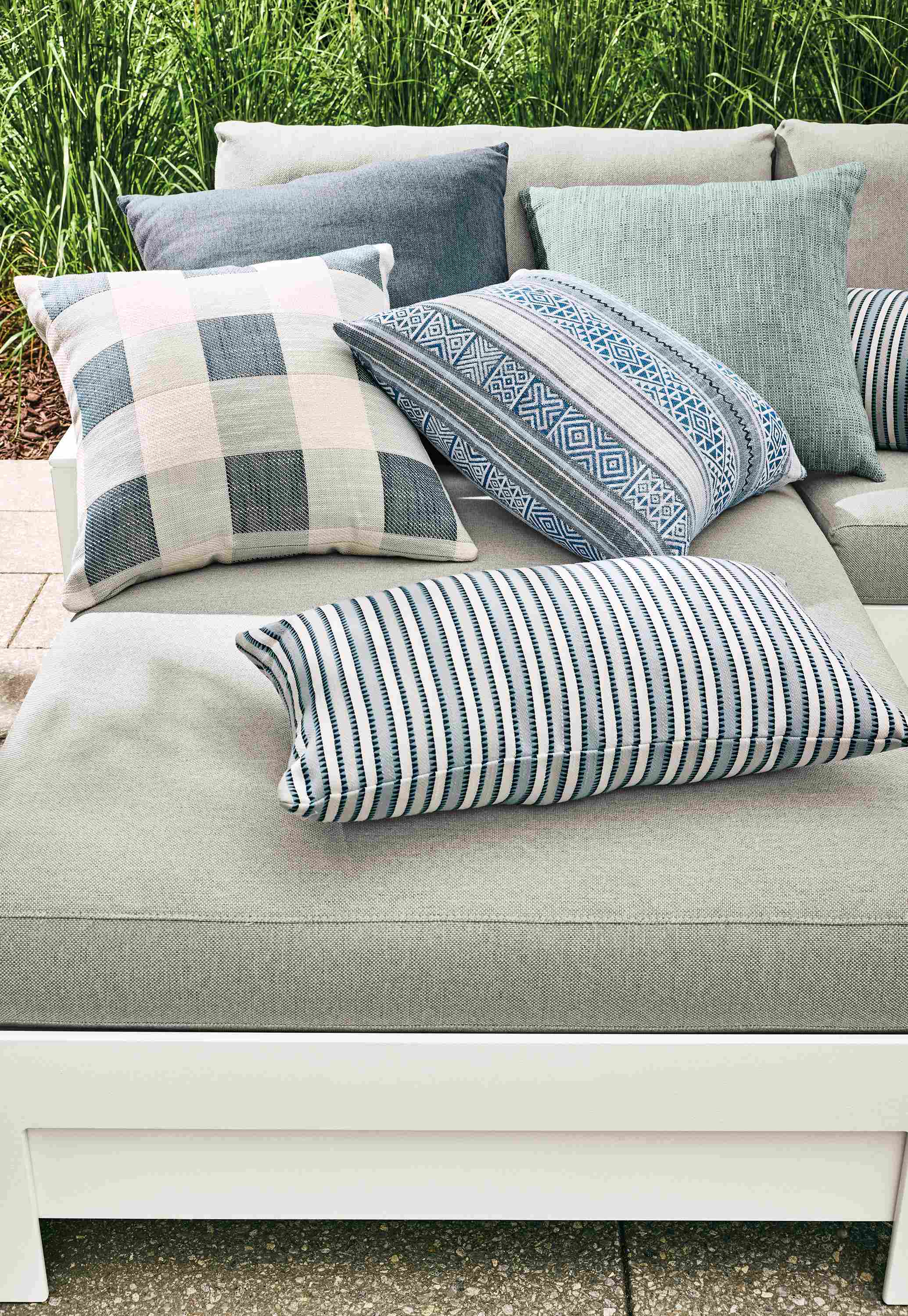 Group of outdoor pillows including suki, cast, yates, estes and pica on a rayo sofa in mist grey.