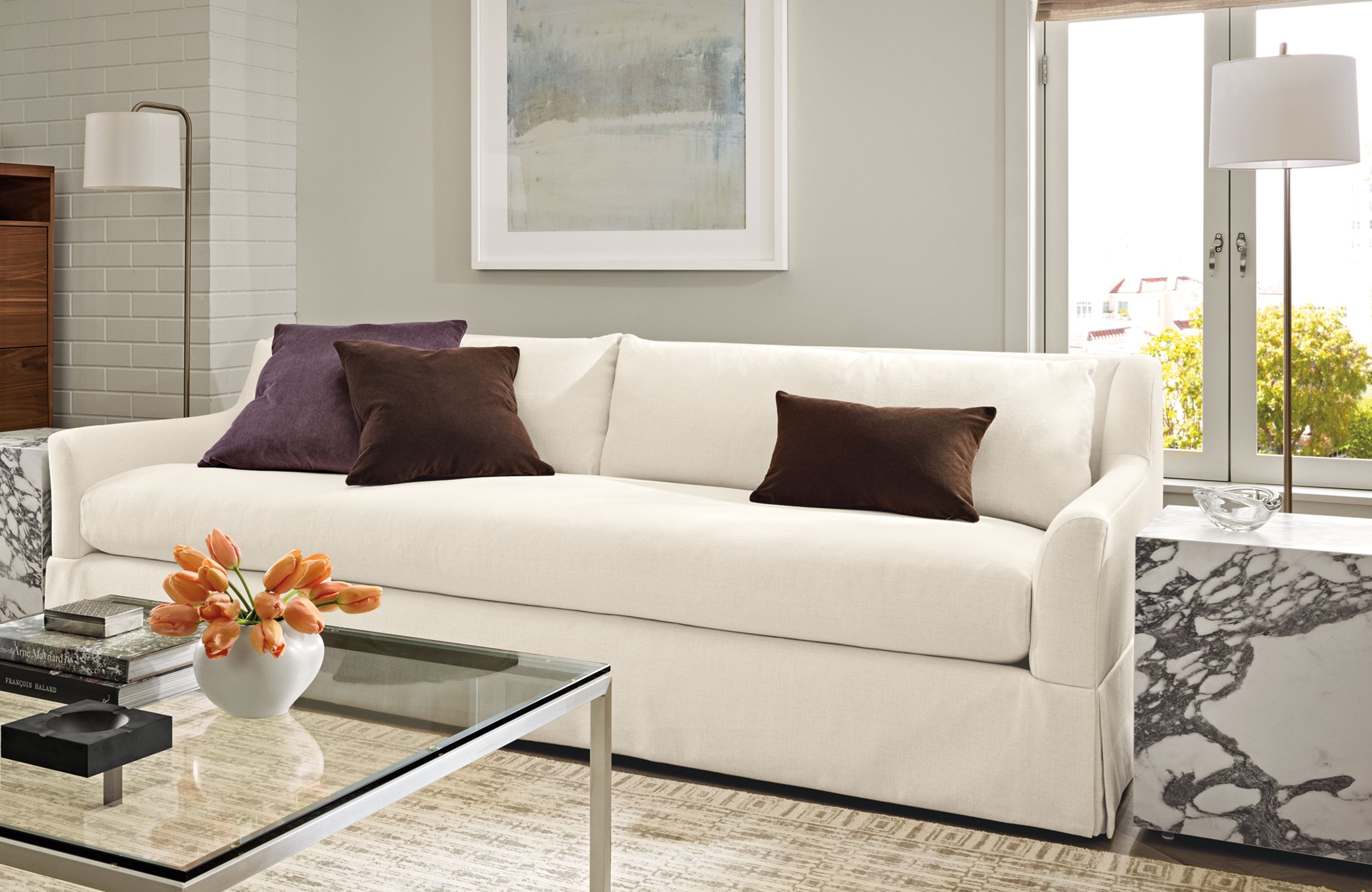 Living room with Sybil 100-wide bench cushion sofa in Sumner Ivory, Parsons coffee table in stainless and clear glass.