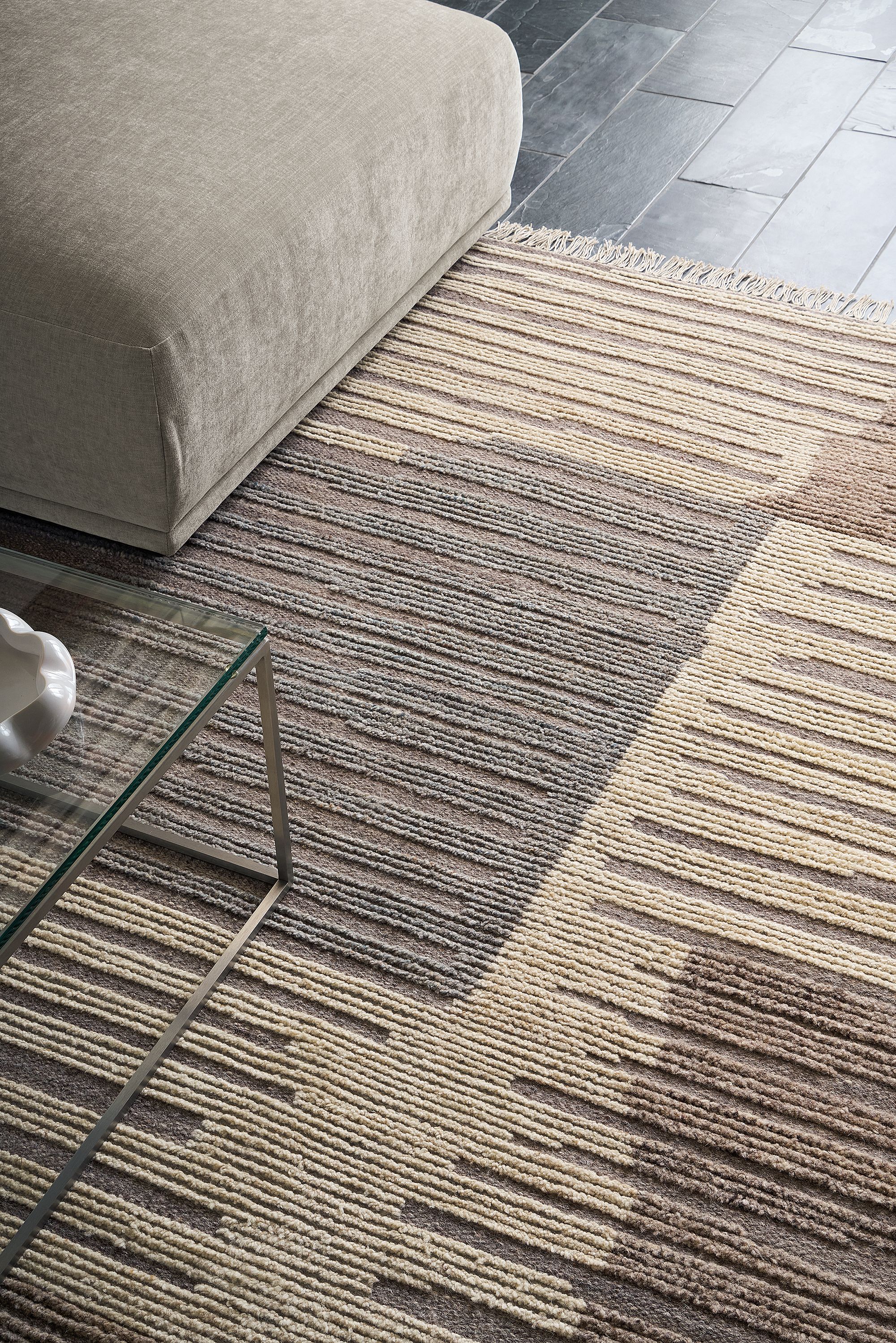 Room with detail of tangier 8 by 10 rug in natural, fia sofa in mori cement and tyne coffee table in clear glass and stainless steel.