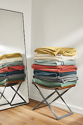 stack of thea matelasse coverlets in a rainbow of colors stacked on bench.
