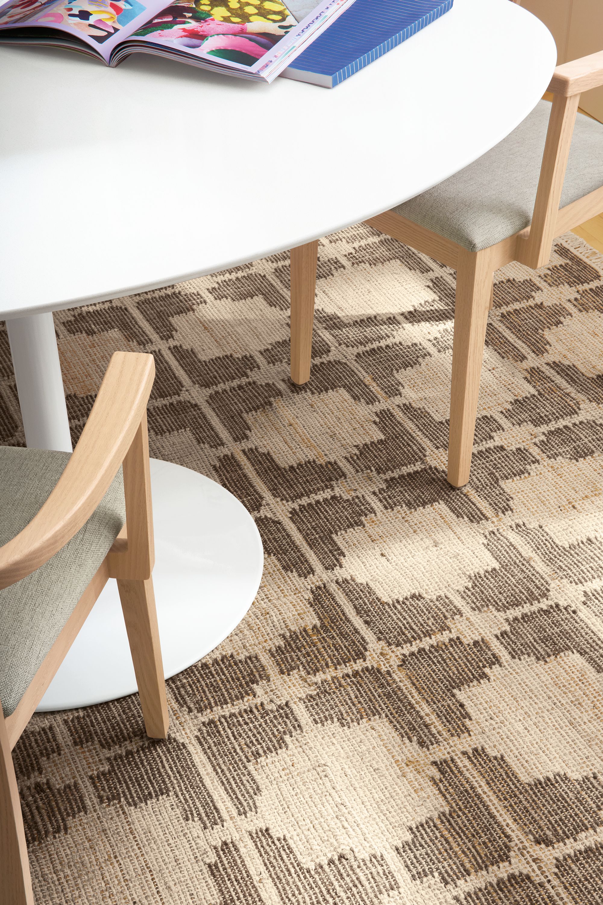 Detail of Tinsley 6 by 9 rug in putty with Aria oval table in white and 2 Doyle arm chairs.