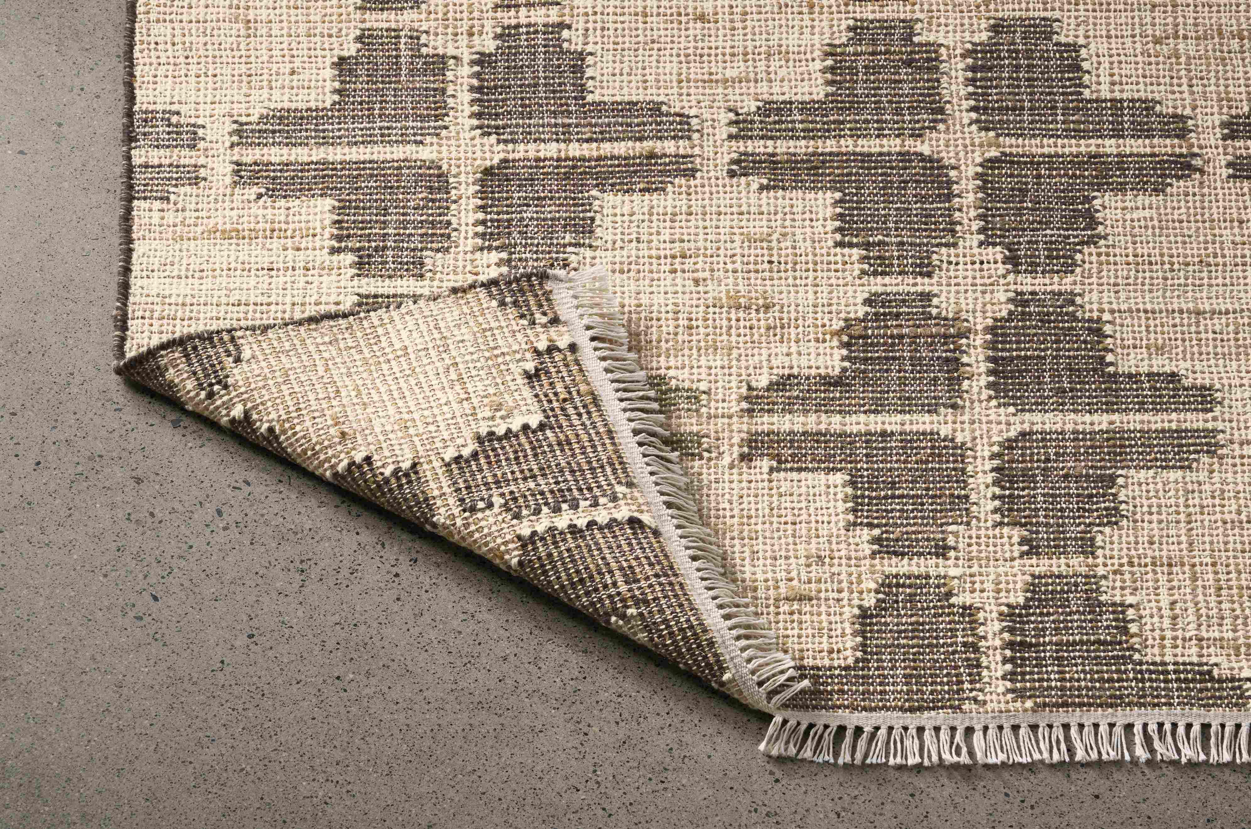 Detail of a Tinsley 8 by 10 rug in putty with corner folded to show underside of rug.