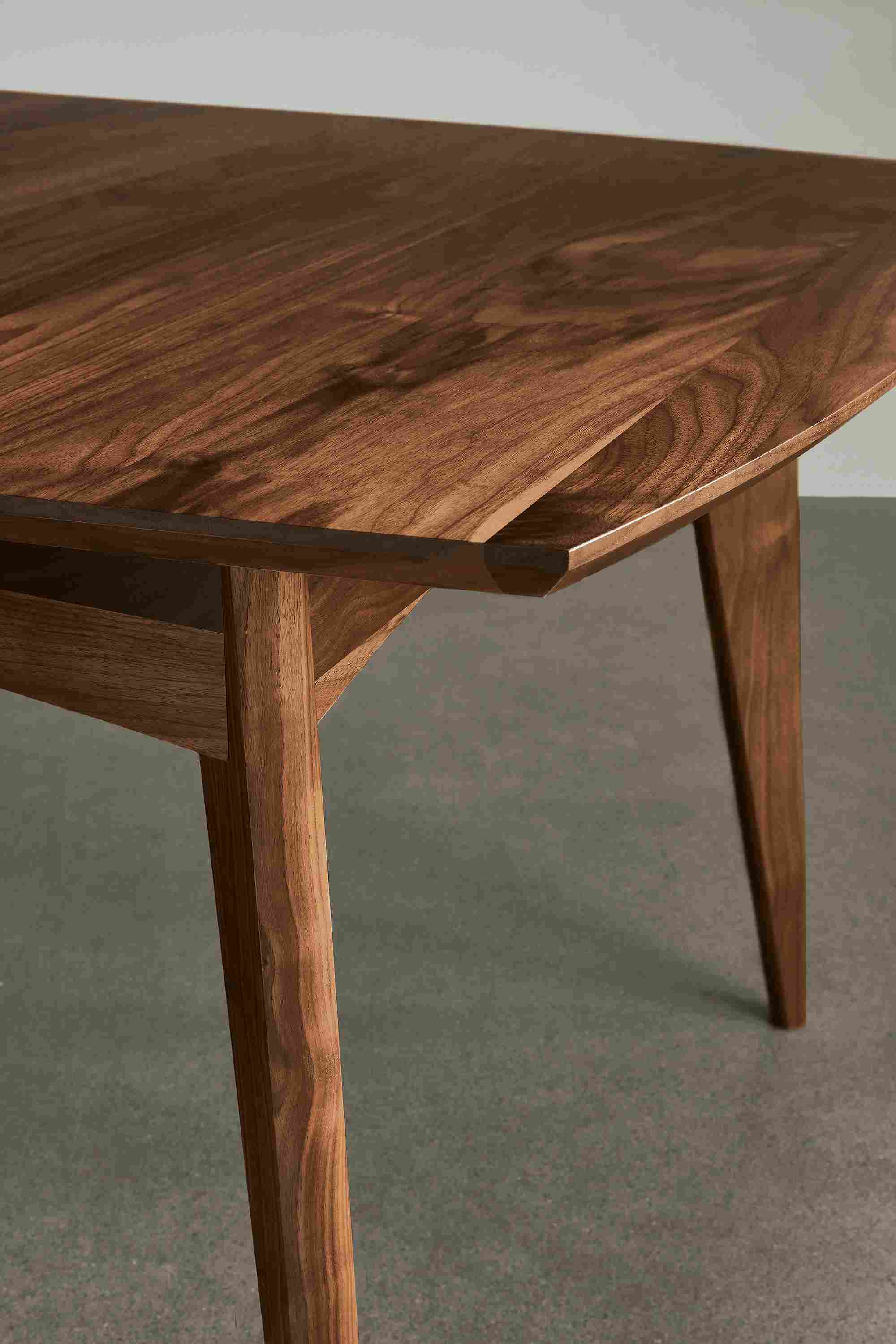 Detail of Ventura extension dining table in walnut standing on a concrete floor.