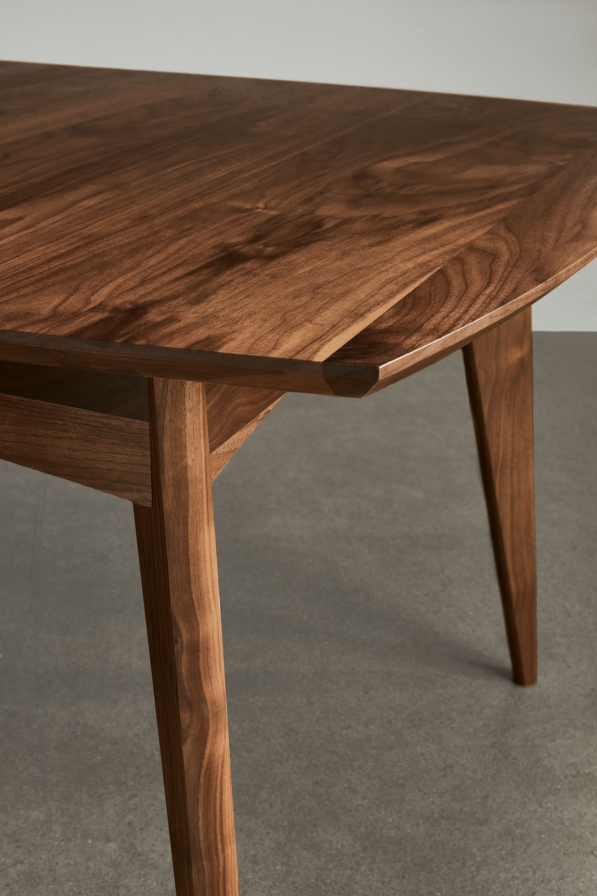 Detail of Ventura extension dining table in walnut standing on a concrete floor.