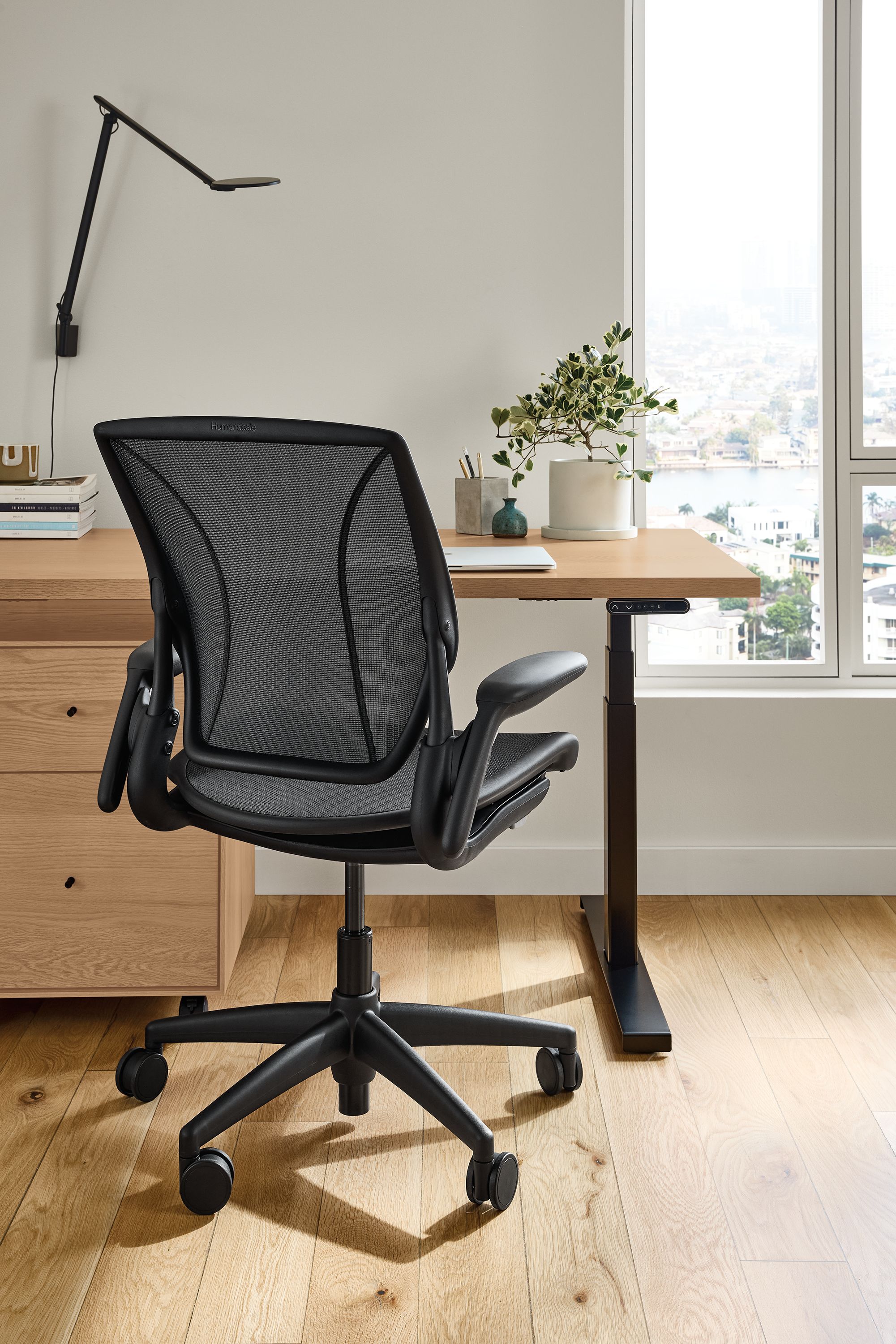 Office area with Wade adjustable standing desk in rye on red oak and a Diffrient World office chair in black mesh.