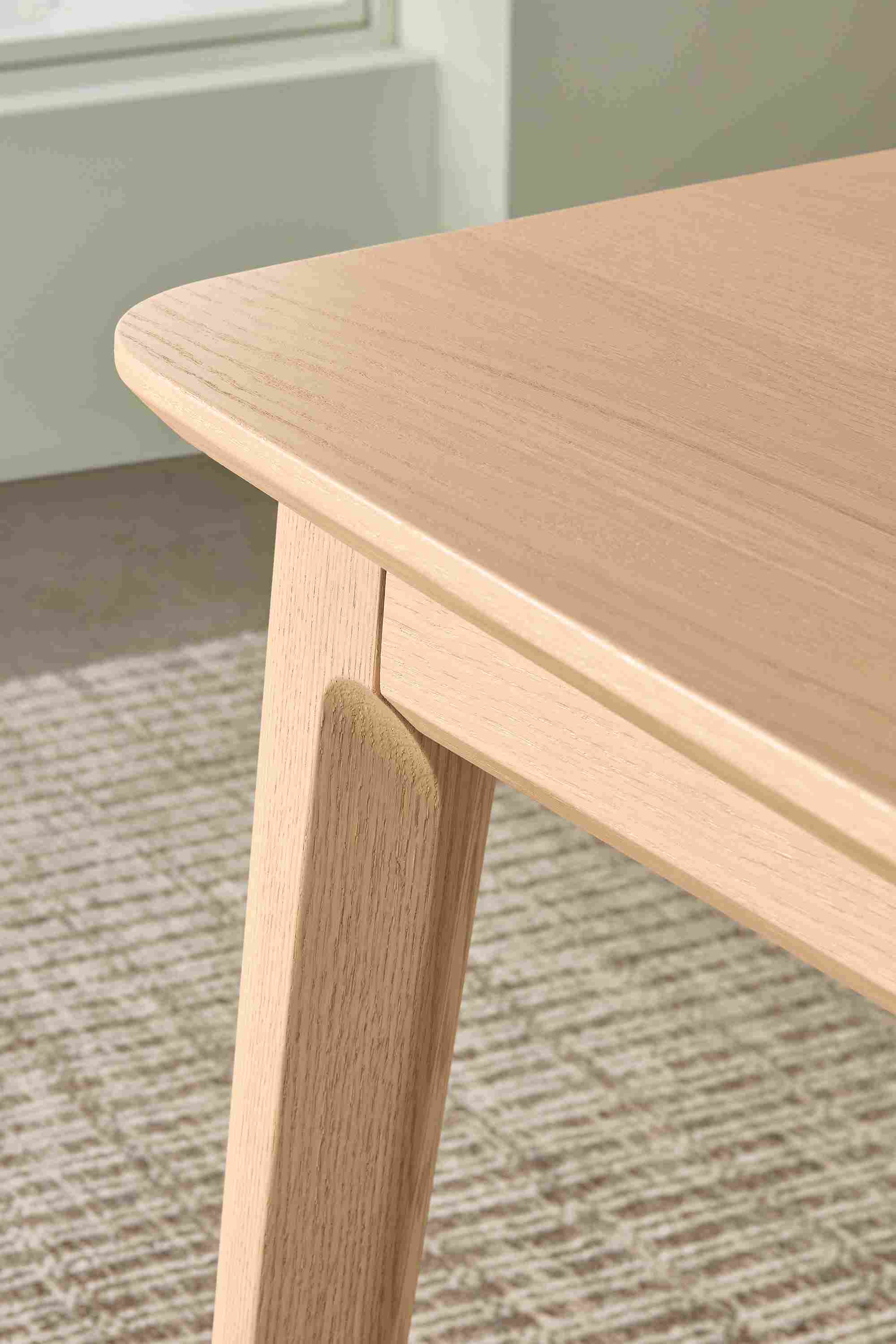 Detail of corner and leg on Walcott 75-wide dining table in salt on red oak and Nera 8 by 10 rug in Stone.