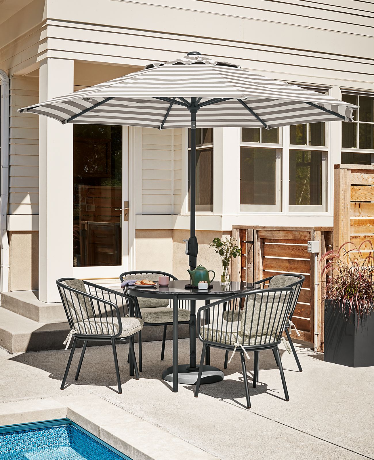 Westbrook 42-round outdoor table with Oahu 9-foot round umbrella in Watts stone and four Delaney chairs in graphite with Phipps taupe cushions.