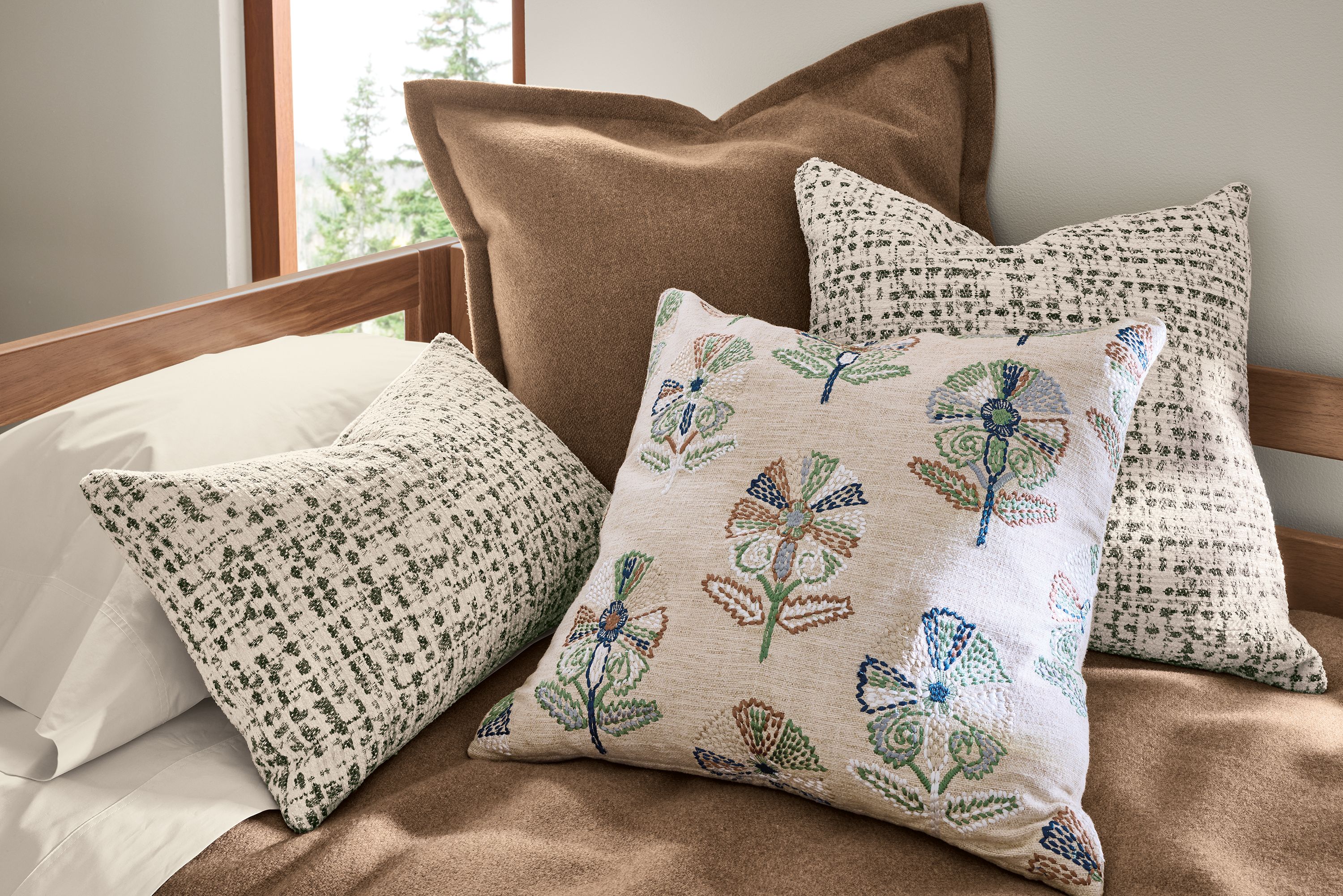 Bed with a group of throw pillows including wister in shale and Tromso in spruce and washable wool sham in camel.