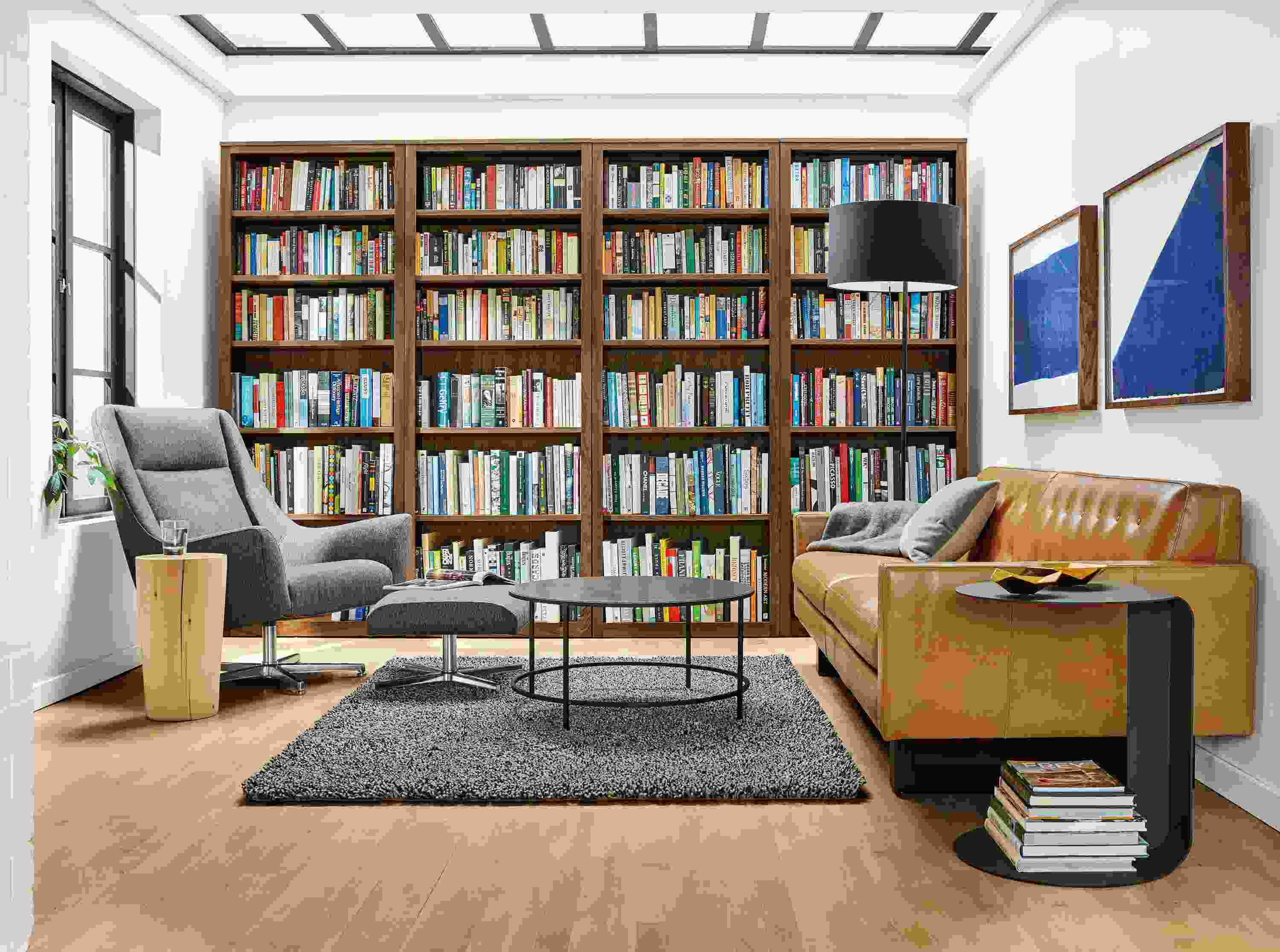 Home library with 4 Woodwind bookcases in walnut, Wells sofa in Brighton Camel and Slim round cocktail table in natural steel.