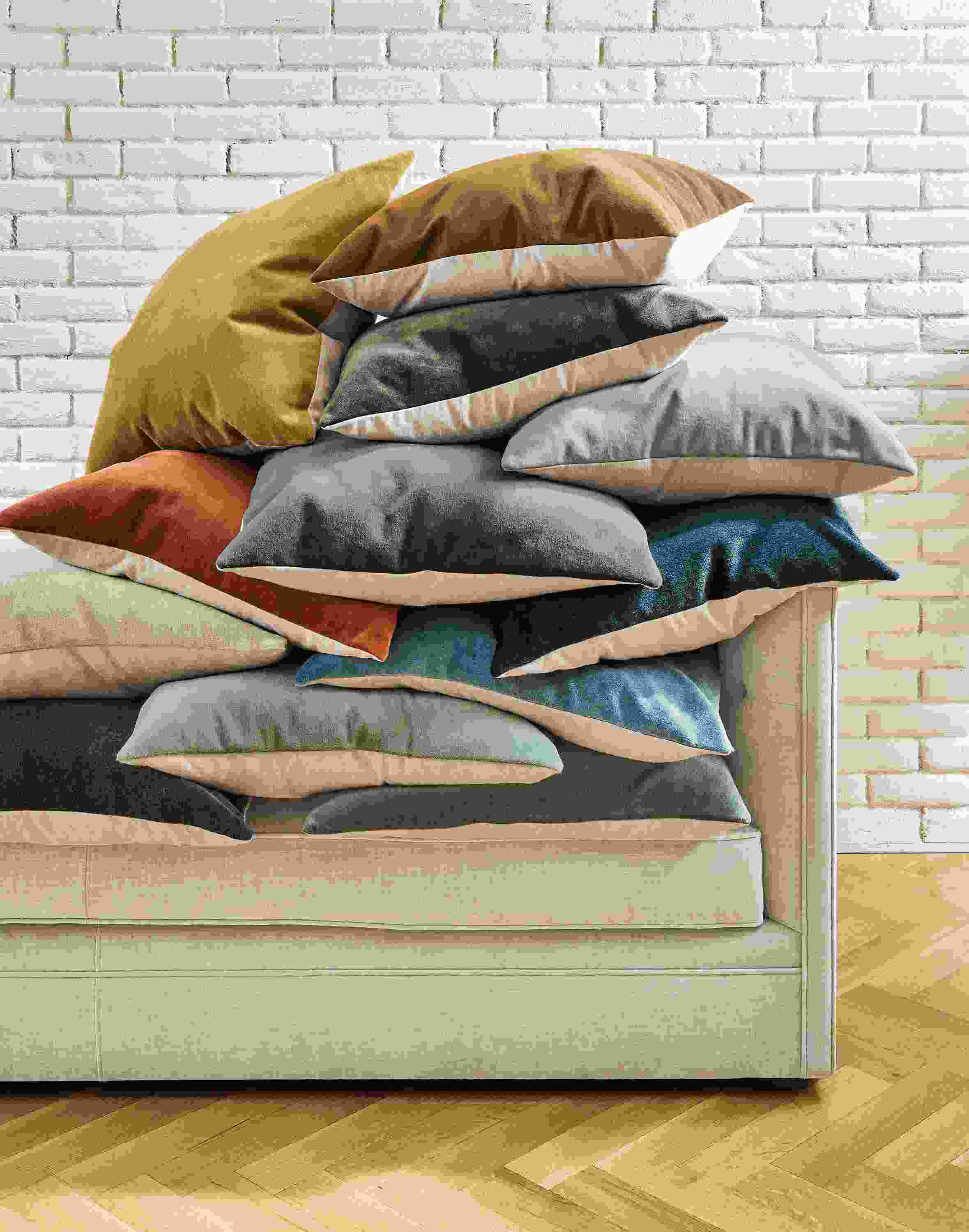 A delightfully messy pile of wool velvet pillows of various colors stacked on a Macalester sofa.