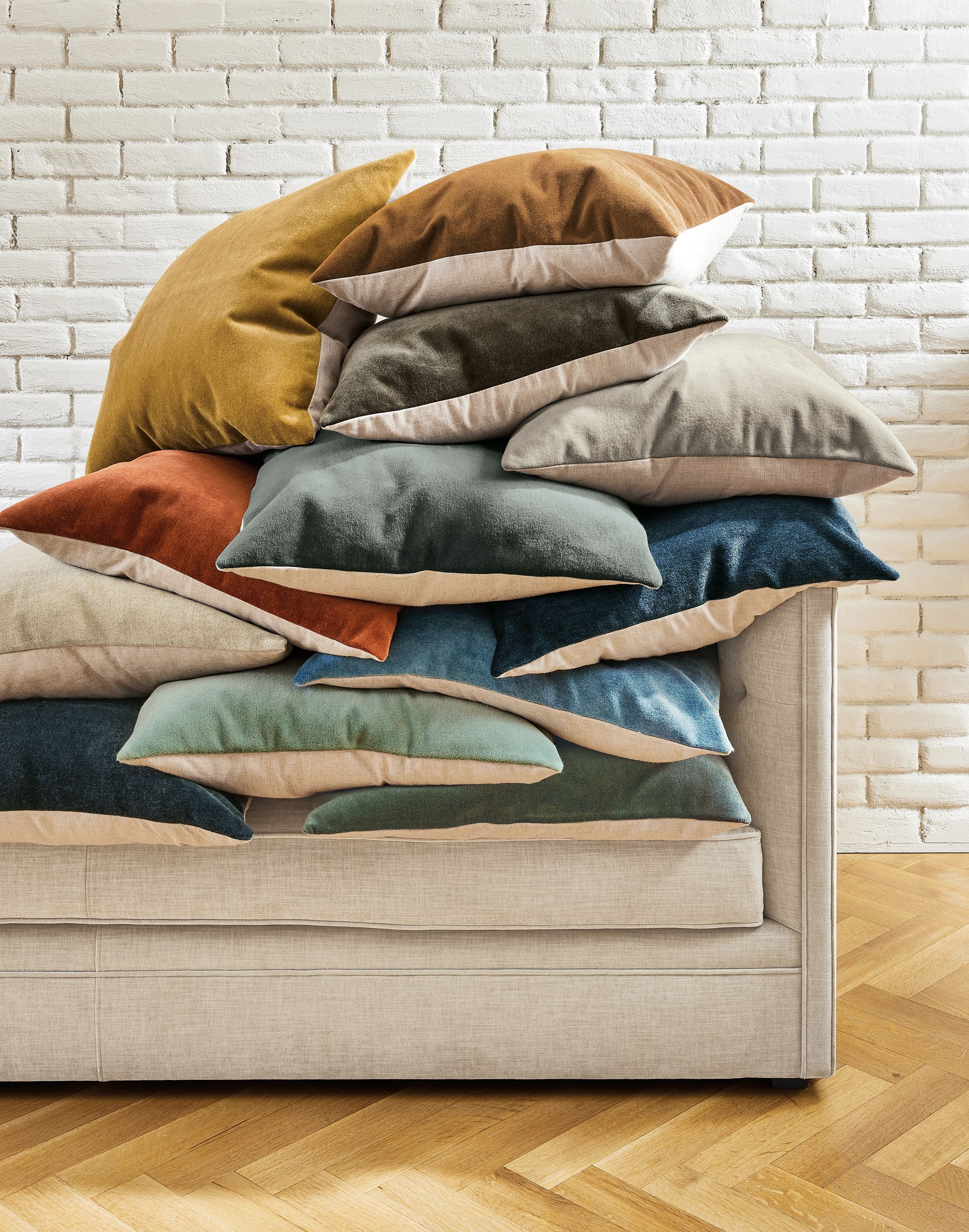 A delightfully messy pile of wool velvet pillows of various colors stacked on a Macalester sofa.